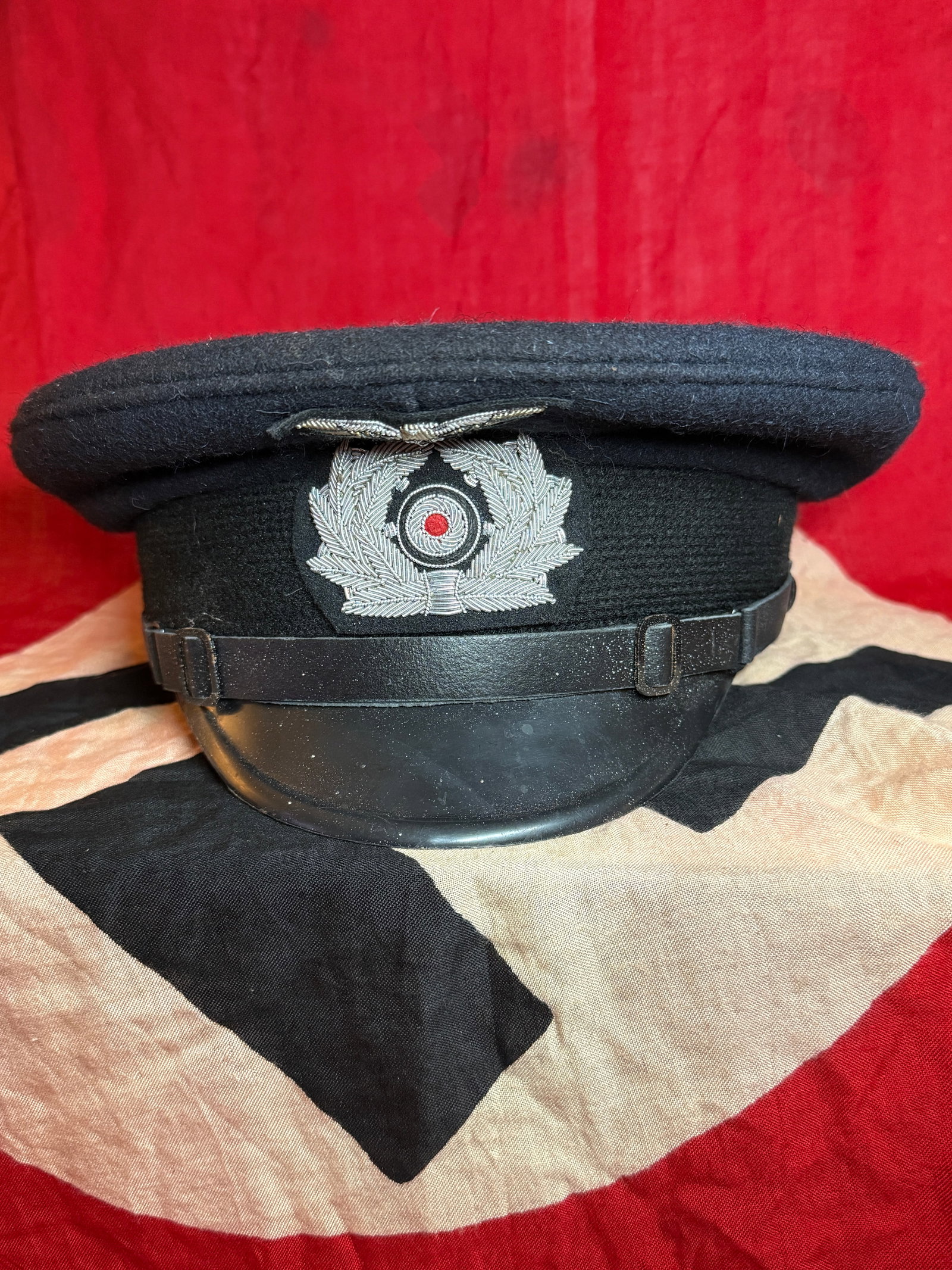 World War II German Police Enlisted Service Visor Cap: Black wool visor cap worn by enlisted personnel and non-commissioned officers of German police organizations during the Second World War. The front displays a silver-colored national cockade surrounde