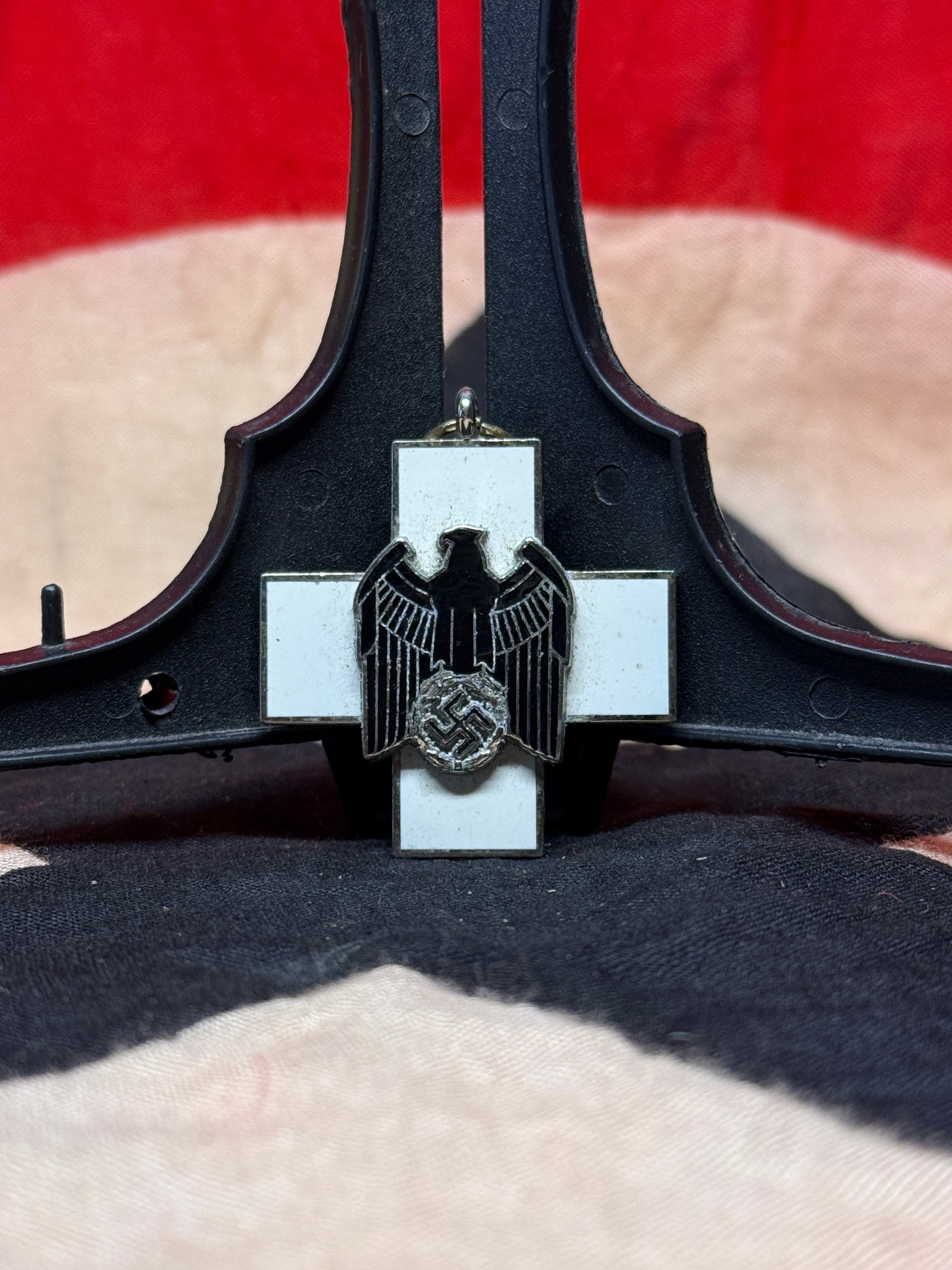 World War II German Social Welfare Decoration Pendant: White enamel cross-shaped pendant featuring a black national eagle with outstretched wings above a wreath motif at the center. Decorations of this type were associated with German social welfare and c