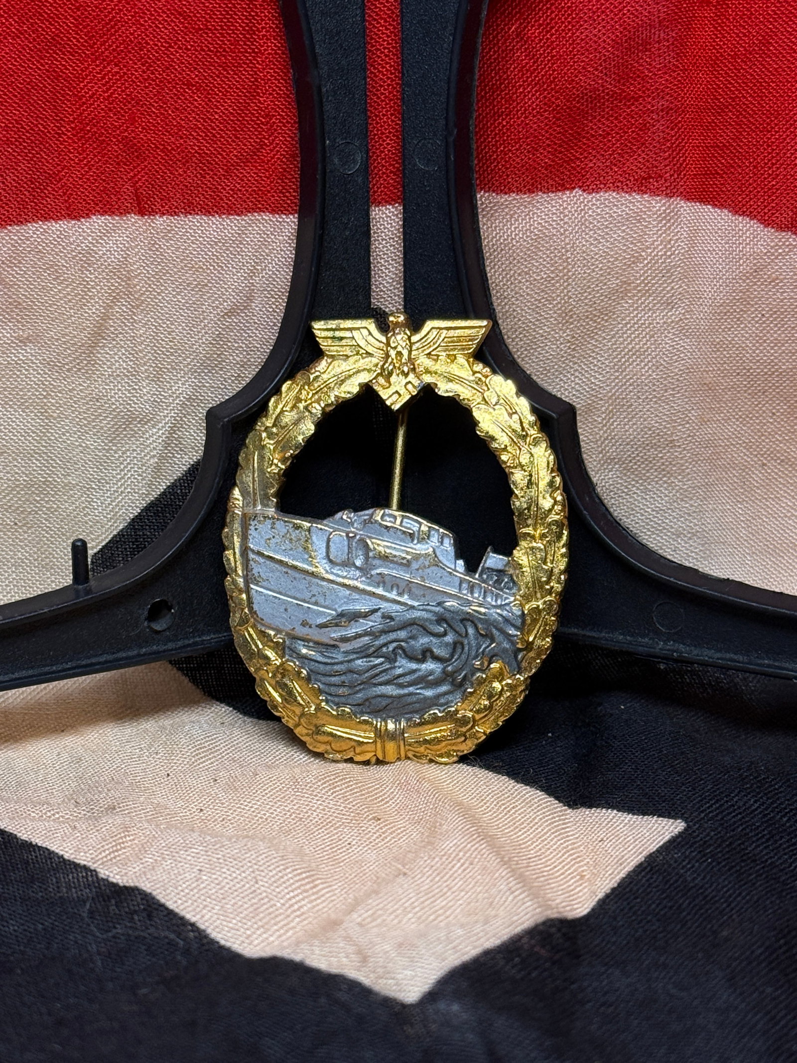 World War II German Kriegsmarine Fast Attack Craft War Badge (Schnellbootkriegsabzeichen): Die-struck Kriegsmarine Fast Attack Craft War Badge depicting a Schnellboot (E-Boat) advancing through stylized waves within an oval oakleaf wreath surmounted by a national eagle. Instituted during th