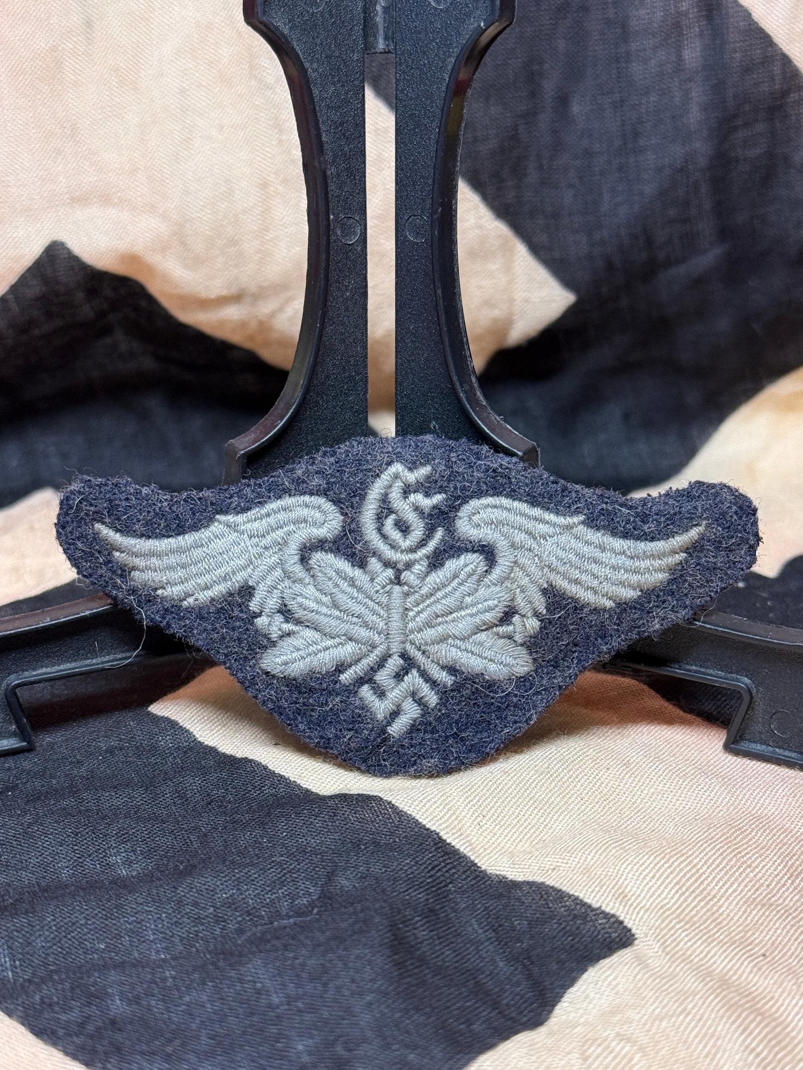 WWII German Luftwaffe Signals Personnel Sleeve Trade Patch: Embroidered Luftwaffe specialty insignia constructed in silver-gray thread on a dark blue wool backing. The design combines stylized wings, a central communications symbol, and an eagle motif associat