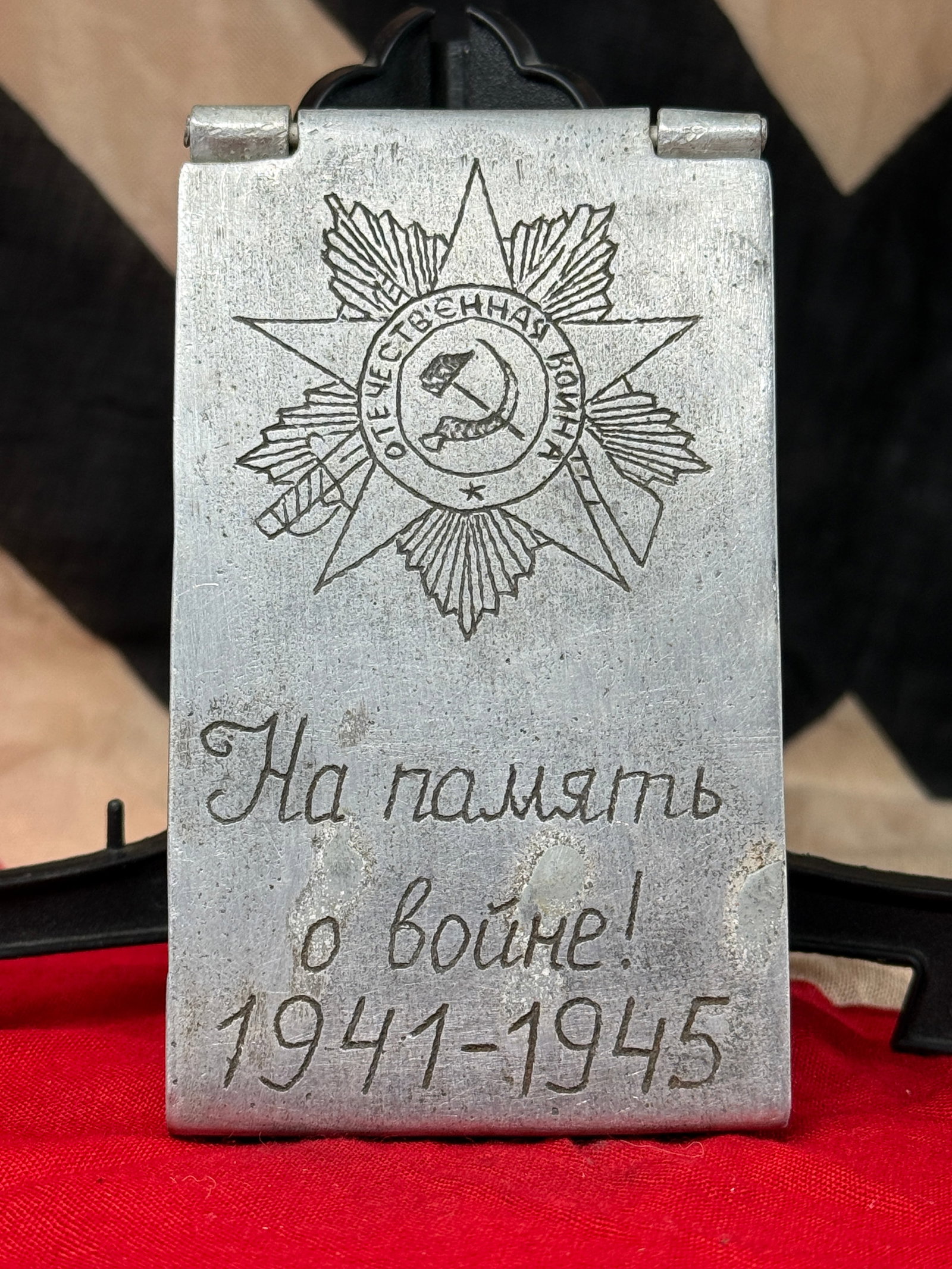 WWII Soviet "In Memory of the War 1941–1945" Aluminum Cigarette Case: This aluminum cigarette case features an engraved Soviet patriotic design on the front depicting the Order of the Patriotic War surrounding the hammer and sickle emblem with the Russian inscription "?