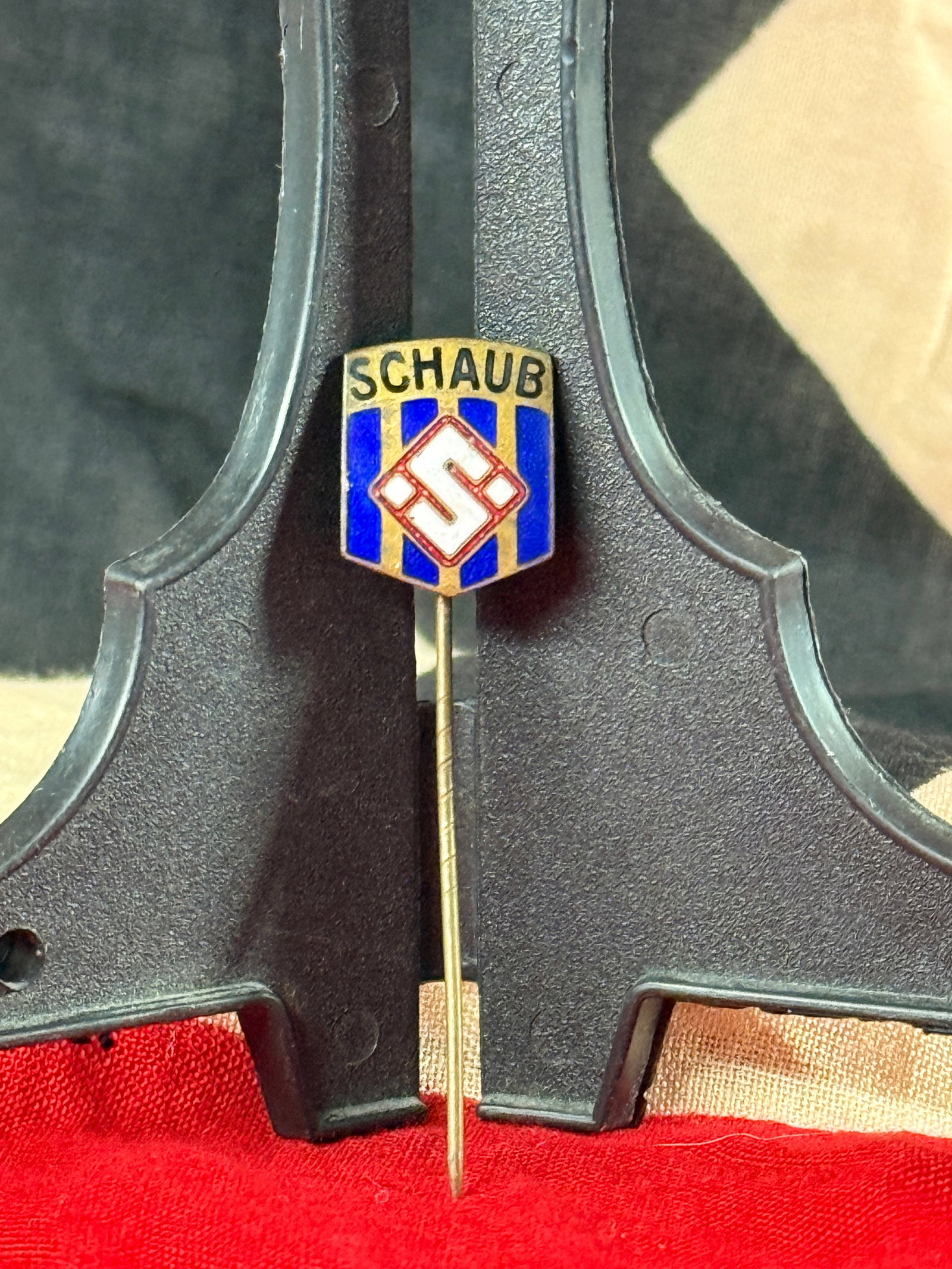 WWII German Hitler Youth "SCHAUB" Enamel Stickpin: This miniature enamel stickpin displays the name “SCHAUB” above a blue-and-gold striped shield with a central Hitler Youth diamond emblem. Constructed of brass with multicolored fired enamel, 