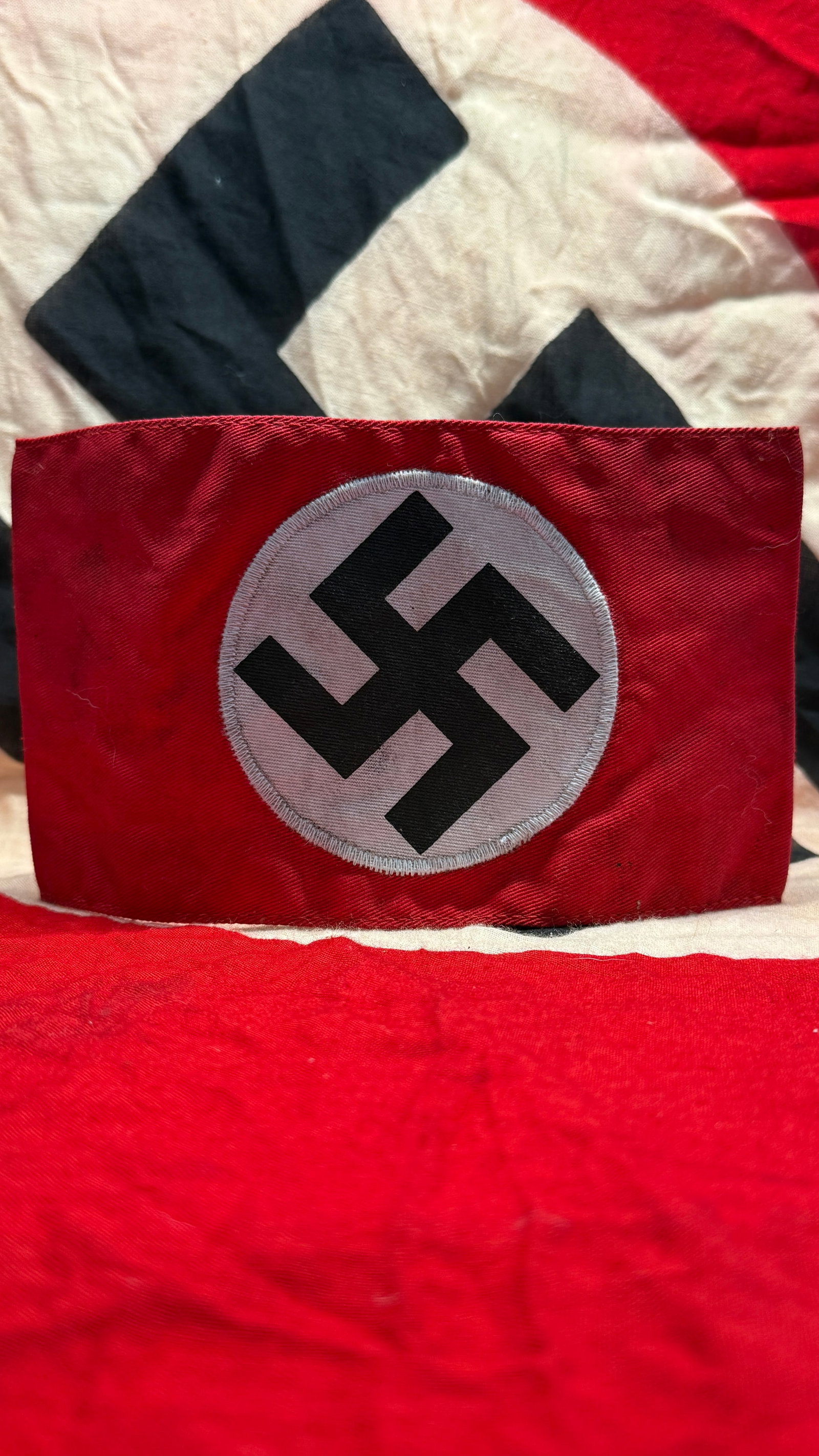 WWII German NSDAP Political Leader Armband with RZM Tag: This red cloth National Socialist German Workers' Party (NSDAP) political leader armband features the centrally applied white roundel with black swastika and retains its interior RZM paper control tag