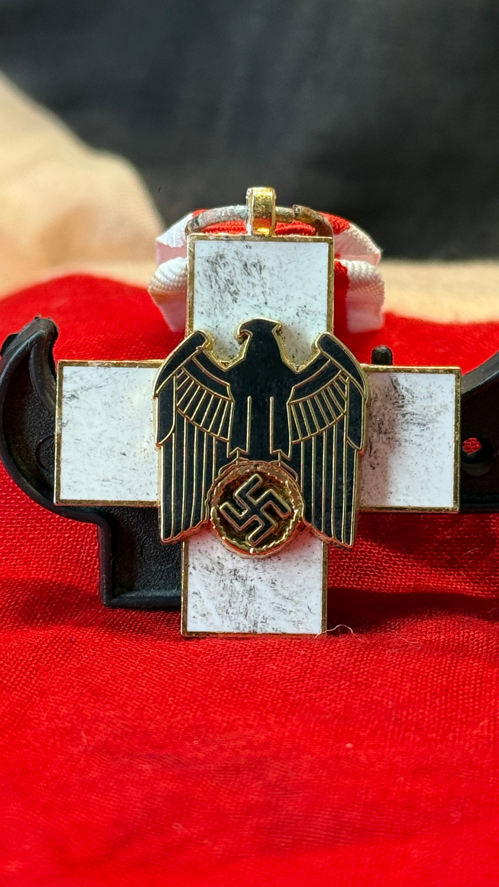 WWII German Social Welfare Decoration 2nd or 3rd Class Cross: This white enamel cross features a black national eagle superimposed over the center with a swastika enclosed by an oak wreath and retains its suspension loop. Instituted by Adolf Hitler on February 1