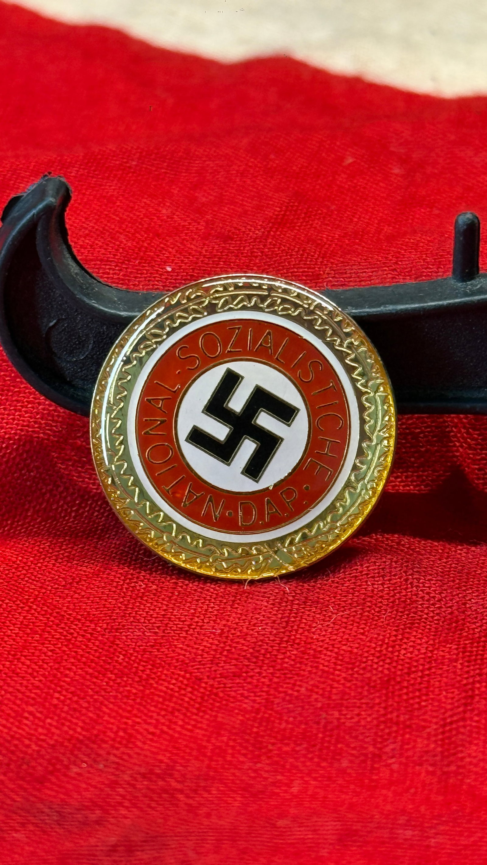 WWII German NSDAP Party Membership Badge: This circular enamel badge displays the black swastika within a white center, surrounded by a red ring bearing the inscription "National-Sozialistische D.A.P." and finished with a decorative gilt bord