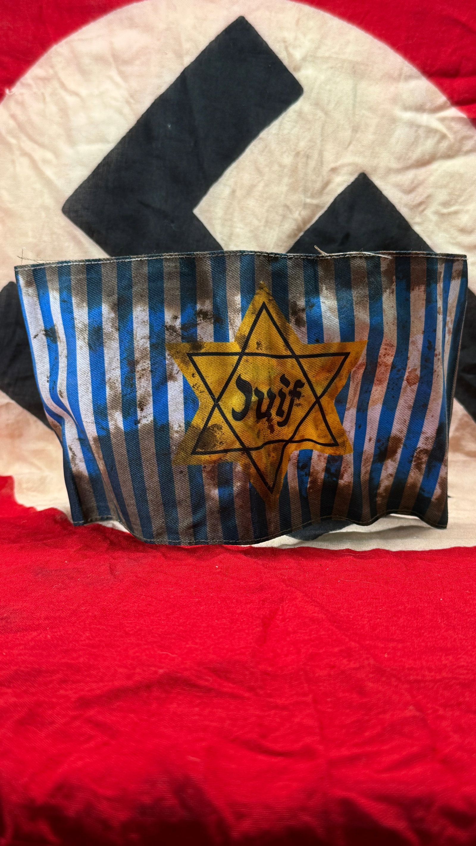 WWII German Concentration Camp Jewish Prisoner Uniform Armband: This striped cloth armband features alternating blue and gray vertical stripes with a yellow Star of David bearing the inscription "Jude" at its center. The construction includes folded and stitched e