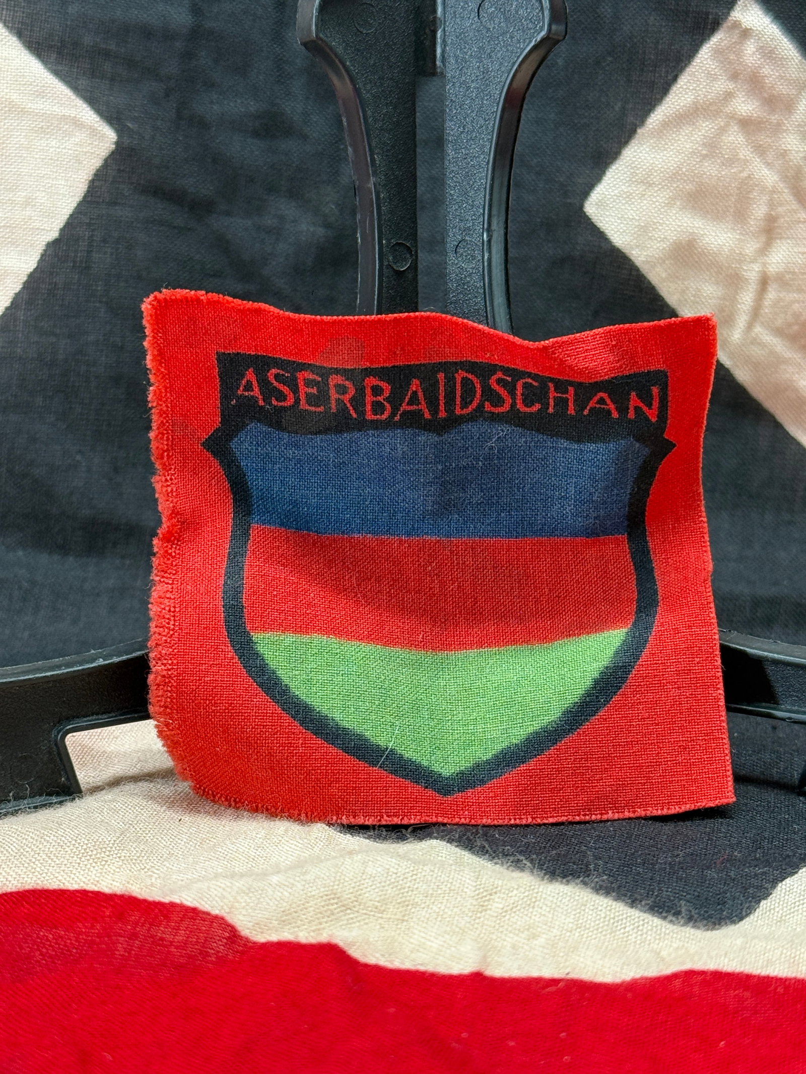 WWII German Azerbaijani Legion (Aserbaidschan) Volunteer Sleeve Shield: This cloth sleeve shield features the tricolor national colors of Azerbaijan beneath the German spelling "ASERBAIDSCHAN" on a red cloth backing. During World War II, volunteer formations composed of A