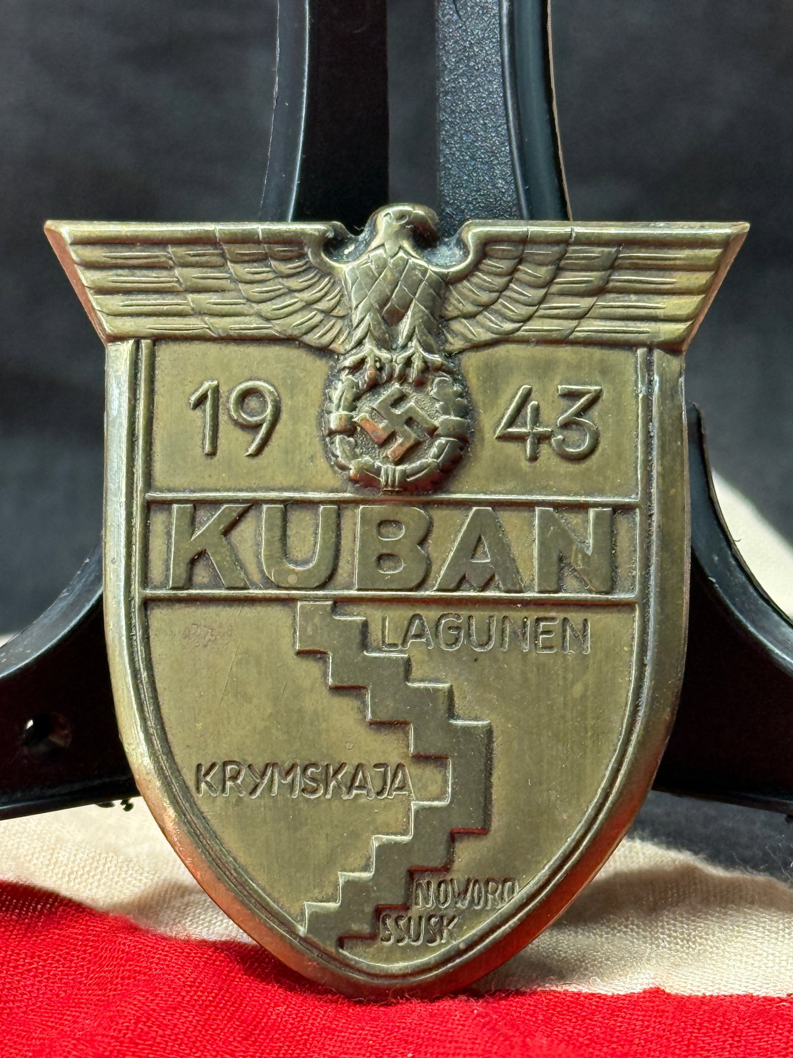 WWII German Kuban Campaign Shield (Kubanschild): This die-struck metal shield bears the Wehrmacht eagle above the date "1943," the word "KUBAN," and the names "Lagunen," "Krymskaja," "Novorossijsk," and the stylized battle line commemorating the Kub