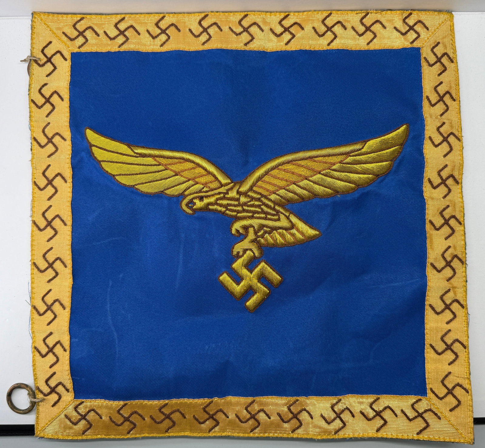 WWII German Luftwaffe Banner Panel with Embroidered Eagle: This World War II German Luftwaffe banner panel features a blue field bordered by a gold embroidered frame decorated with repeating swastika motifs and a large gold Luftwaffe eagle clutching a swastik