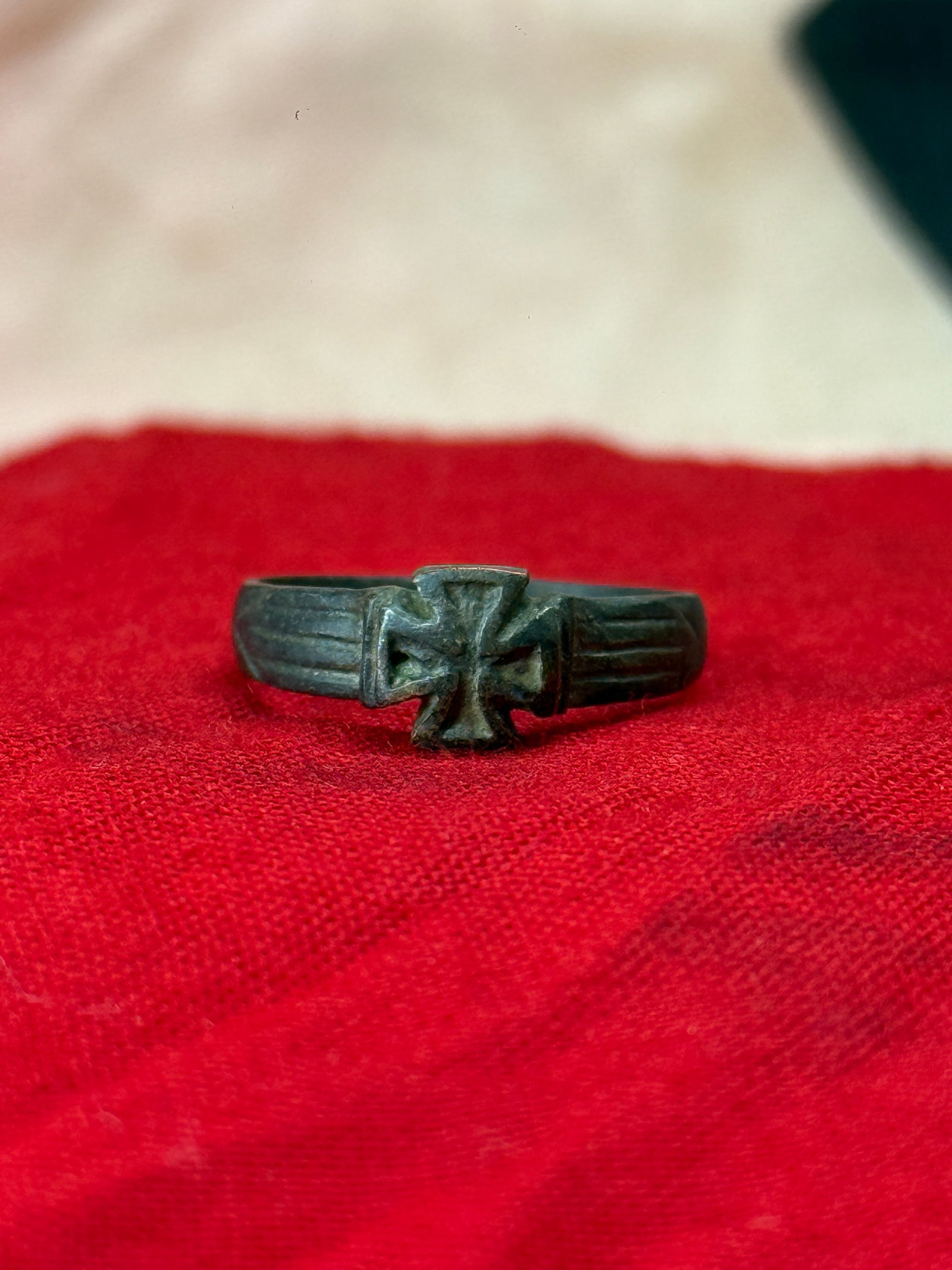 WWII German Iron Cross Ring: This dark metal finger ring features the iconic Iron Cross prominently displayed on its bezel with fluted shoulders extending along each side of the band. Rings of this style became popular patriotic 