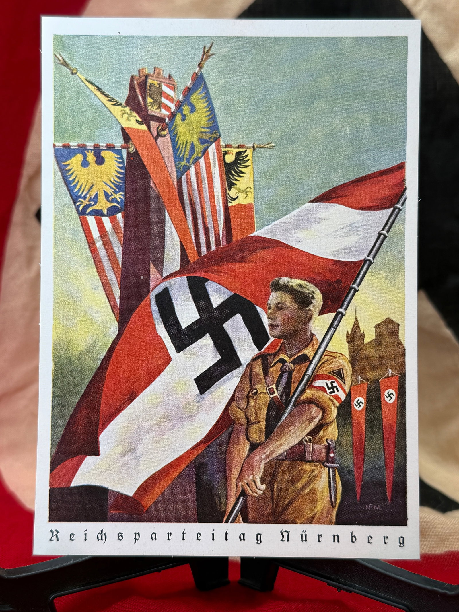 WWII German Reichsparteitag Nürnberg Hitler Youth Propaganda Postcard: This printed propaganda postcard depicts a Hitler Youth standard bearer carrying the National Socialist flag before a grouping of Reich banners beneath the caption "Reichsparteitag Nürnberg." Produce