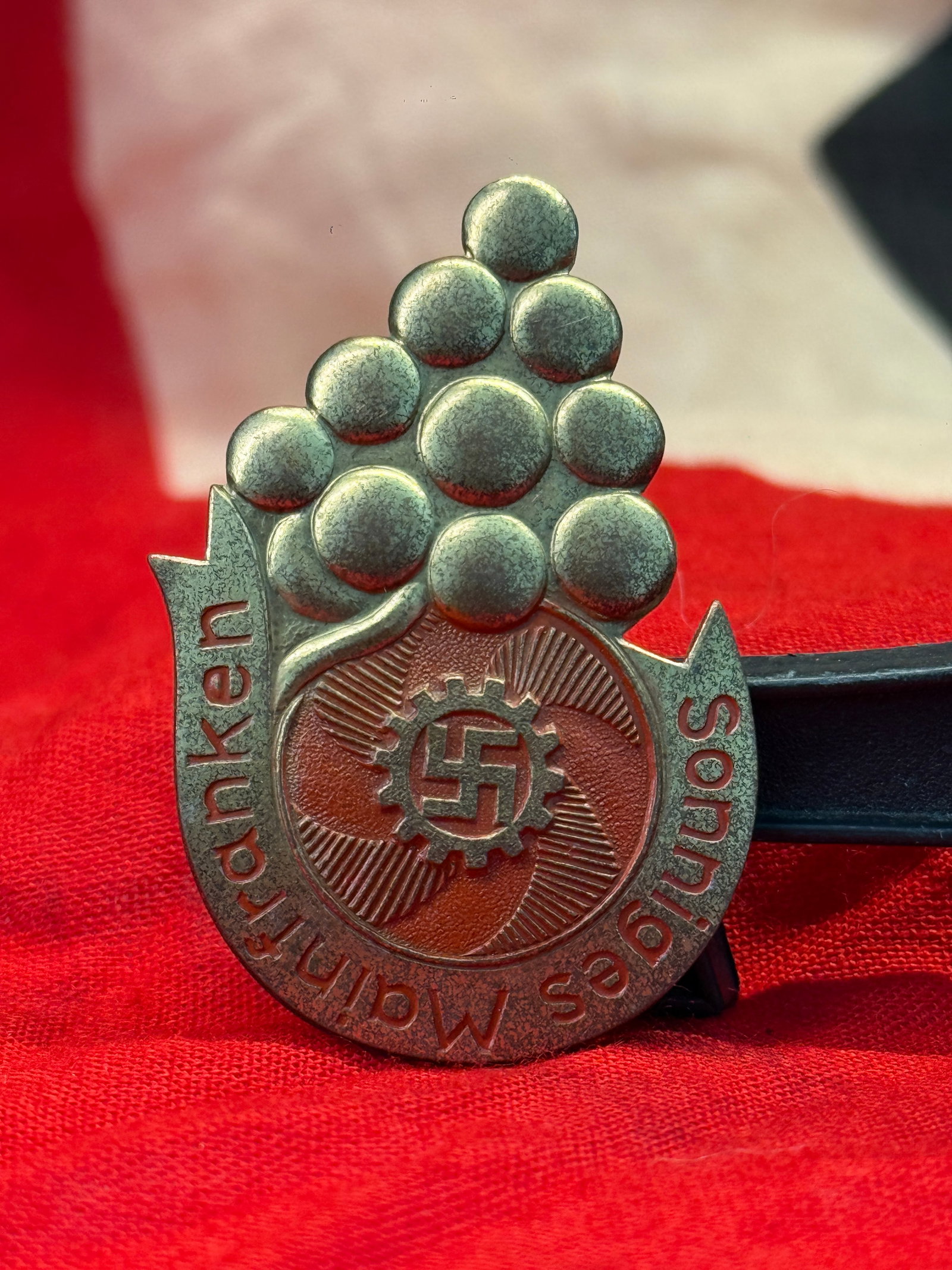 WWII German Kraft durch Freude (KdF) Souvenir Tinnie Badge: Die-struck metal Kraft durch Freude (Strength Through Joy) souvenir tinnie featuring a cluster of grapes above the KdF cogwheel-and-swastika emblem with "Mainfranken Souvenir" incorporated into the de