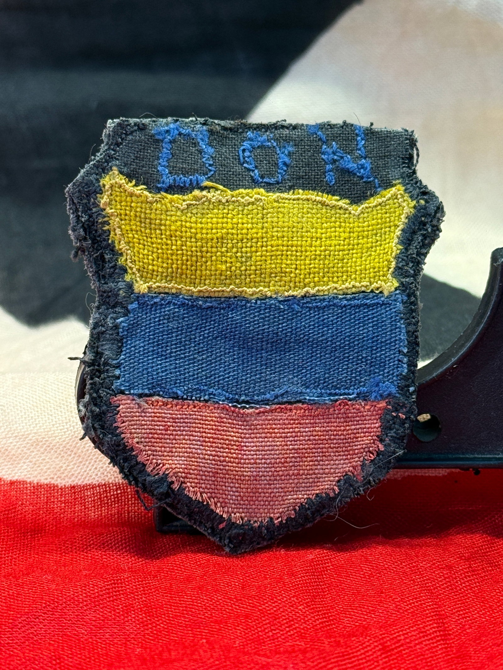 WWII German Volunteer Sleeve Shield ("DON"): Shield-shaped cloth sleeve insignia embroidered with the word "DON" above horizontal yellow, blue, and red stripes, mounted on a dark wool backing. The reverse shows period-style stitching and constru