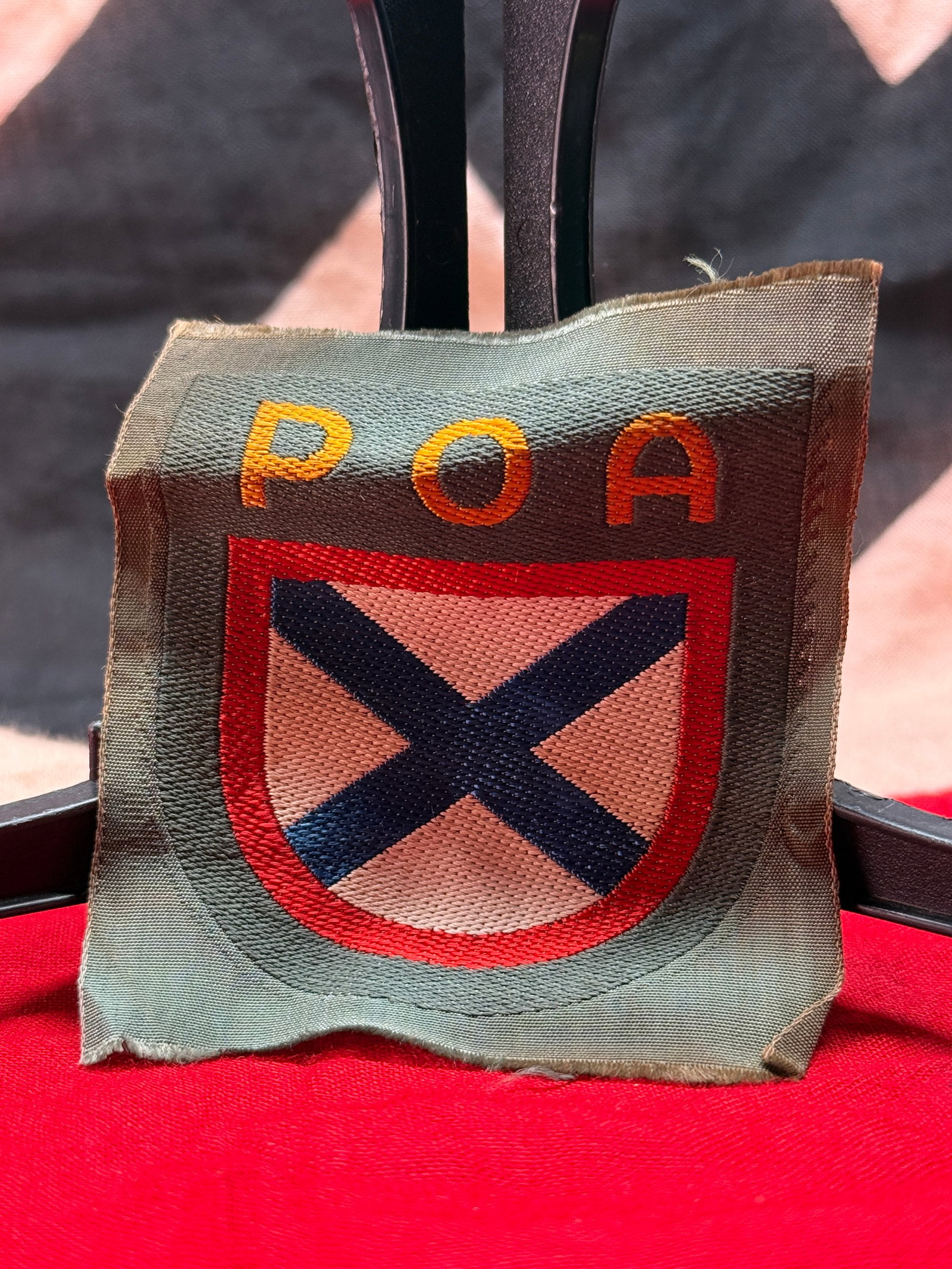 WWII German Ordnungspolizei (Order Police) "POA" Sleeve Insignia: This embroidered cloth sleeve insignia features the gold letters "POA" above a heraldic shield displaying a black saltire bordered in red on a light-colored field. Woven in multicolored thread on a po