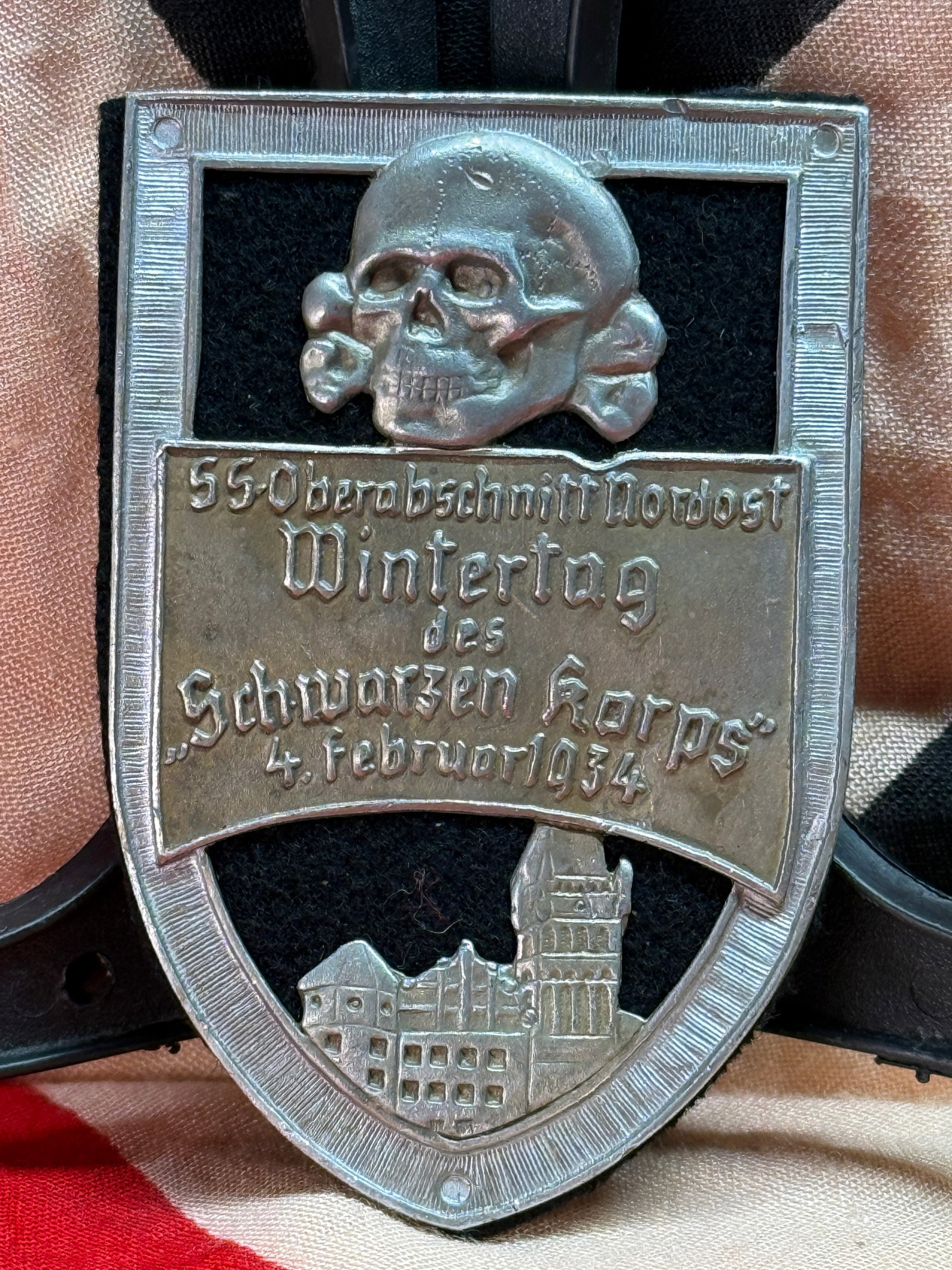 WWII German SS Oberabschnitt Nordost "Wintertag des Schwarzen Korps" 1934 Tinnie: This pressed metal commemorative tinnie bears an SS Totenkopf above the inscription "SS Oberabschnitt Nordost Wintertag des Schwarzen Korps 4. Februar 1934." The lower section depicts an architectural