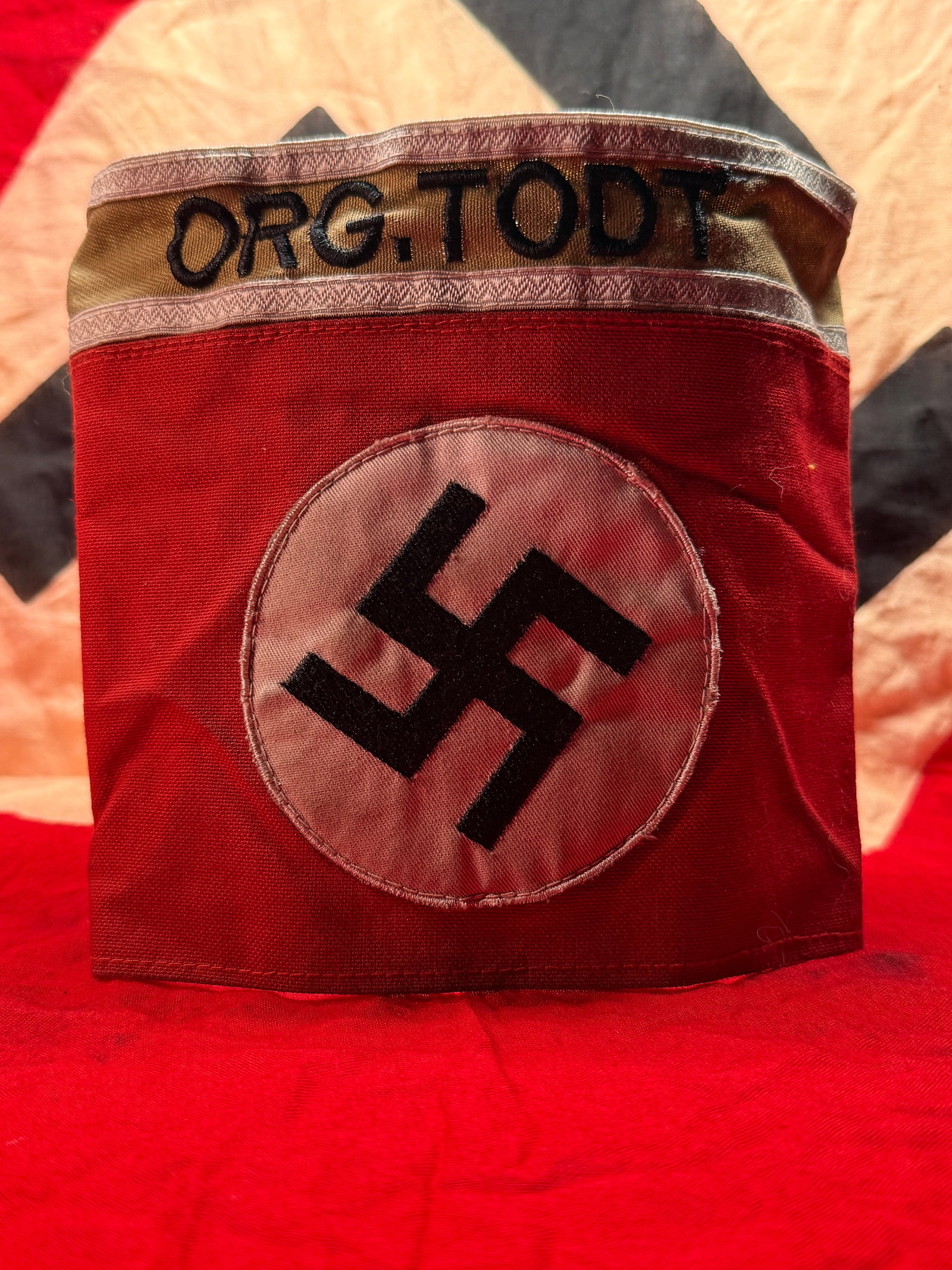 WWII German Organisation Todt (OT) Armband: This red cloth armband features a white roundel with a black swastika and is embroidered across the tan upper band with the designation "ORG. TODT." Organisation Todt served as the Third Reich's princ