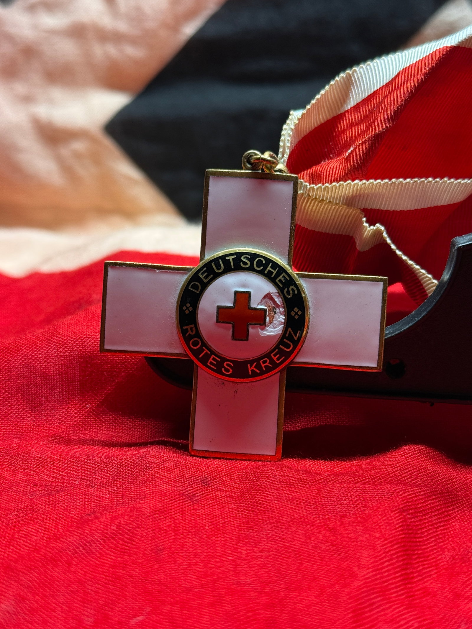 WWII German Red Cross (Deutsches Rotes Kreuz) Honor Decoration: This white enameled cross bears the inscription "DEUTSCHES ROTES KREUZ" surrounding a red enamel cross at its center and is suspended from its original red and white neck ribbon. Decorations of this s