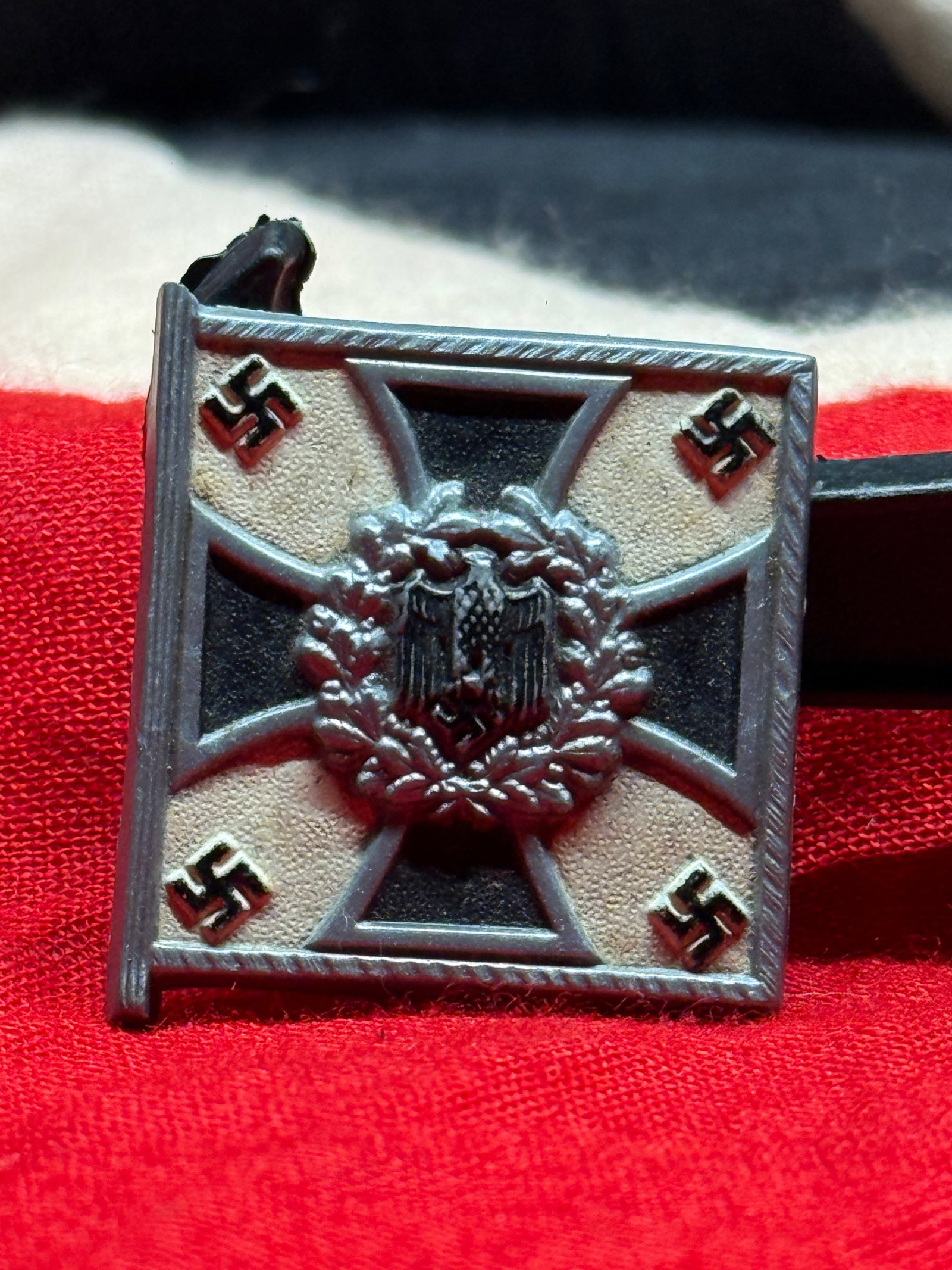 WWII German Flag-Themed Veterans or Patriotic Tinnie Badge: This WWII-era German patriotic tinnie-style badge features a raised Iron Cross-inspired flag design with national eagle and wreath detail at the center. The reverse has a pin-back attachment and molde