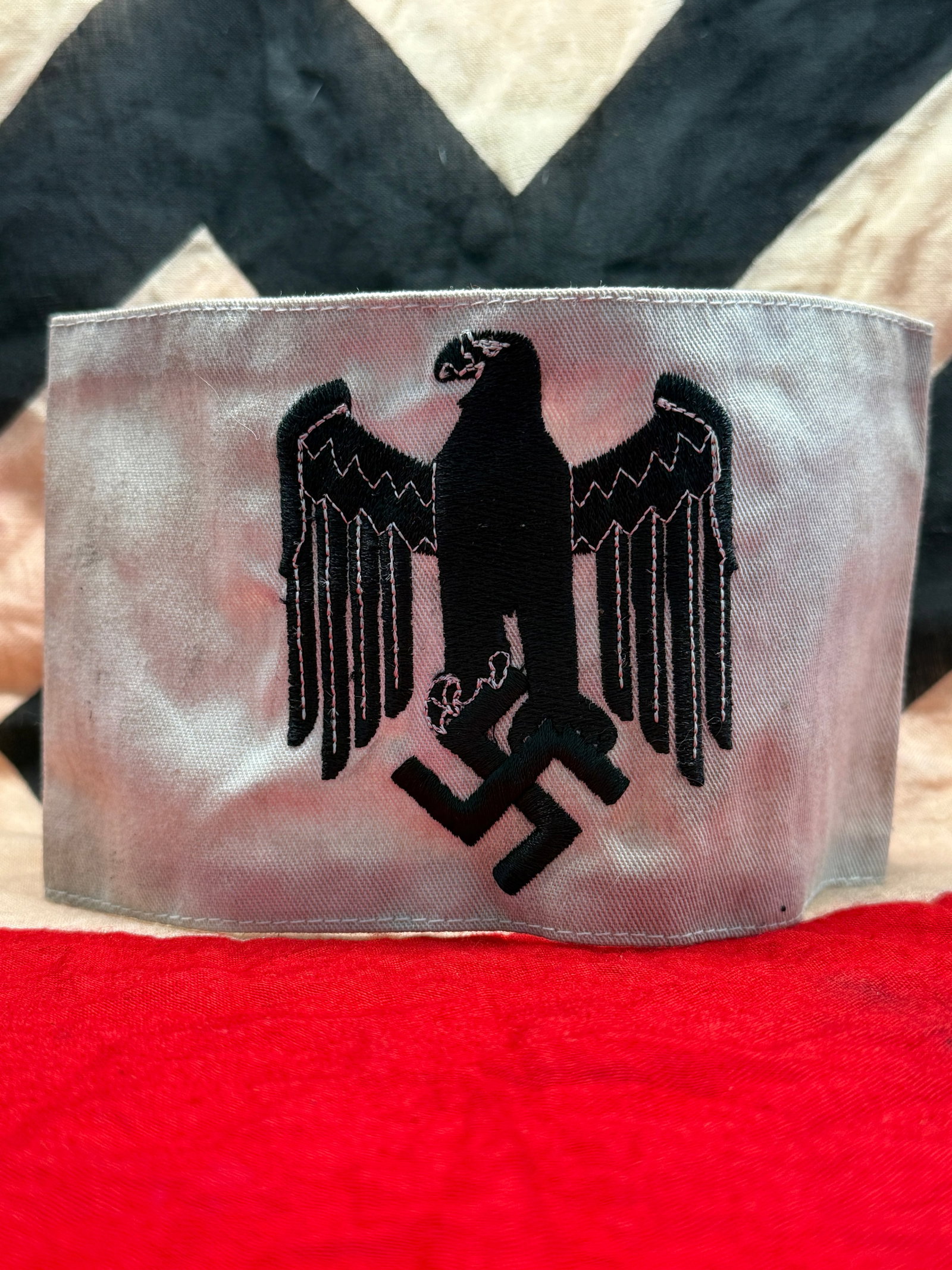 WWII German Wehrmacht Eagle Armband: This white cloth armband is embroidered with the German national eagle clutching a swastika in black thread, a design associated with the Wehrmacht during the Second World War. Armbands of this patter