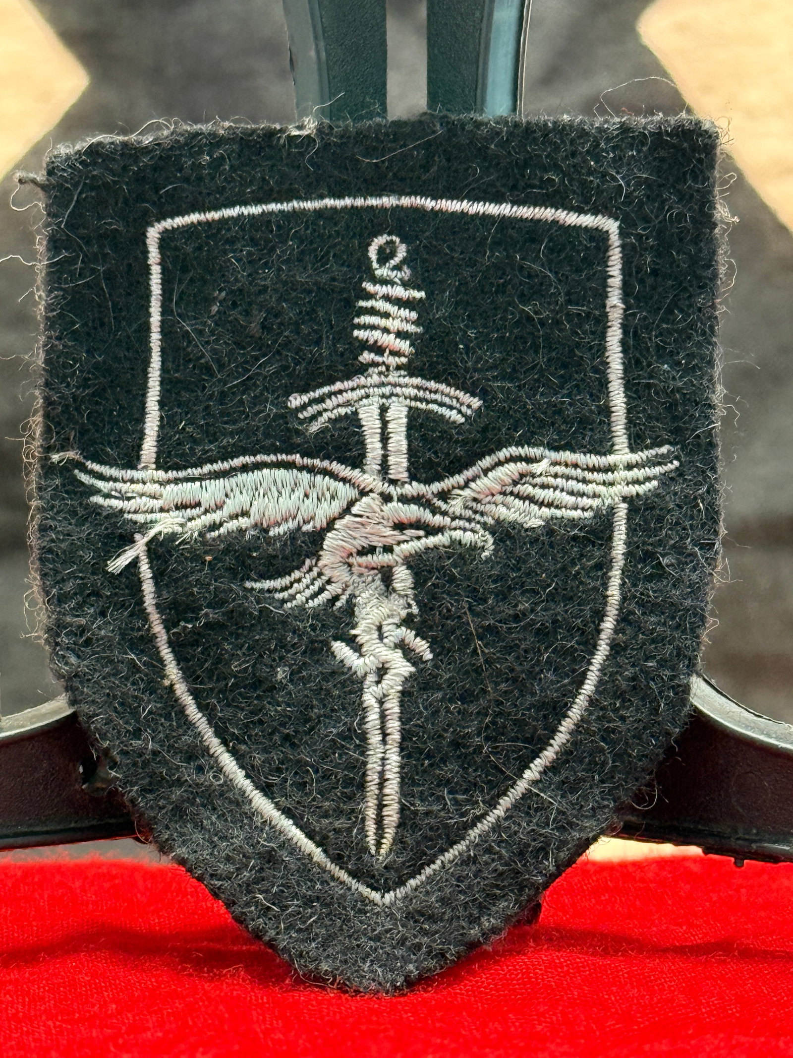 WWII German Waffen-SS Medical Sleeve Diamond: This black wool Waffen-SS sleeve diamond features finely machine-embroidered silver-gray thread depicting a sword entwined by a serpent, enclosed within a shield-shaped border. The serpent and sword m