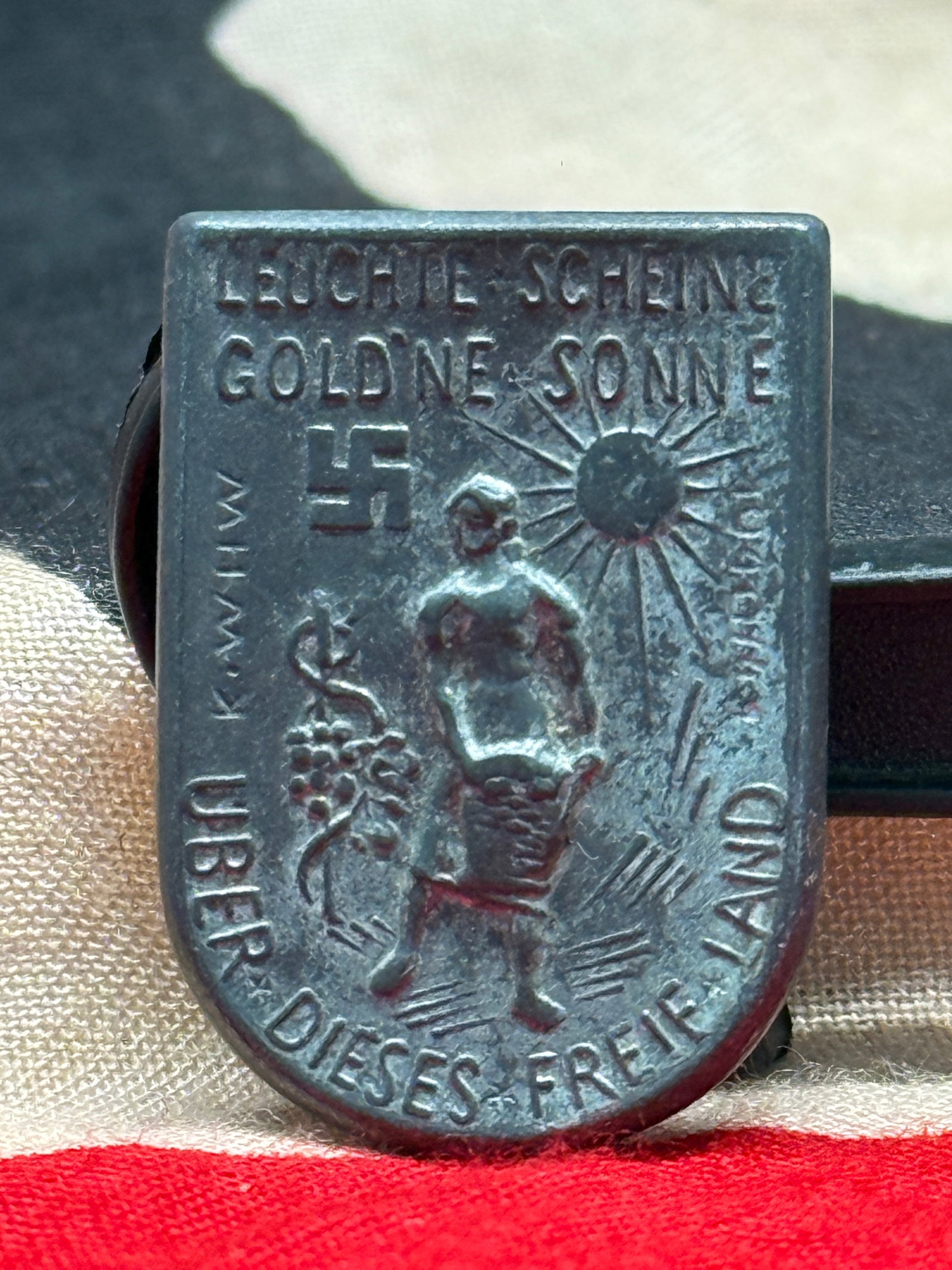 WWII German Winterhilfswerk (WHW) 1940/41 "Leuchte-Scheine Goldne Sonne" Tinnie: This WWII German Winterhilfswerk (WHW) commemorative tinnie bears the inscription "Leuchte-Scheine Goldne Sonne Über Dieses Freie Land" surrounding a scene depicting a laborer carrying a basket benea