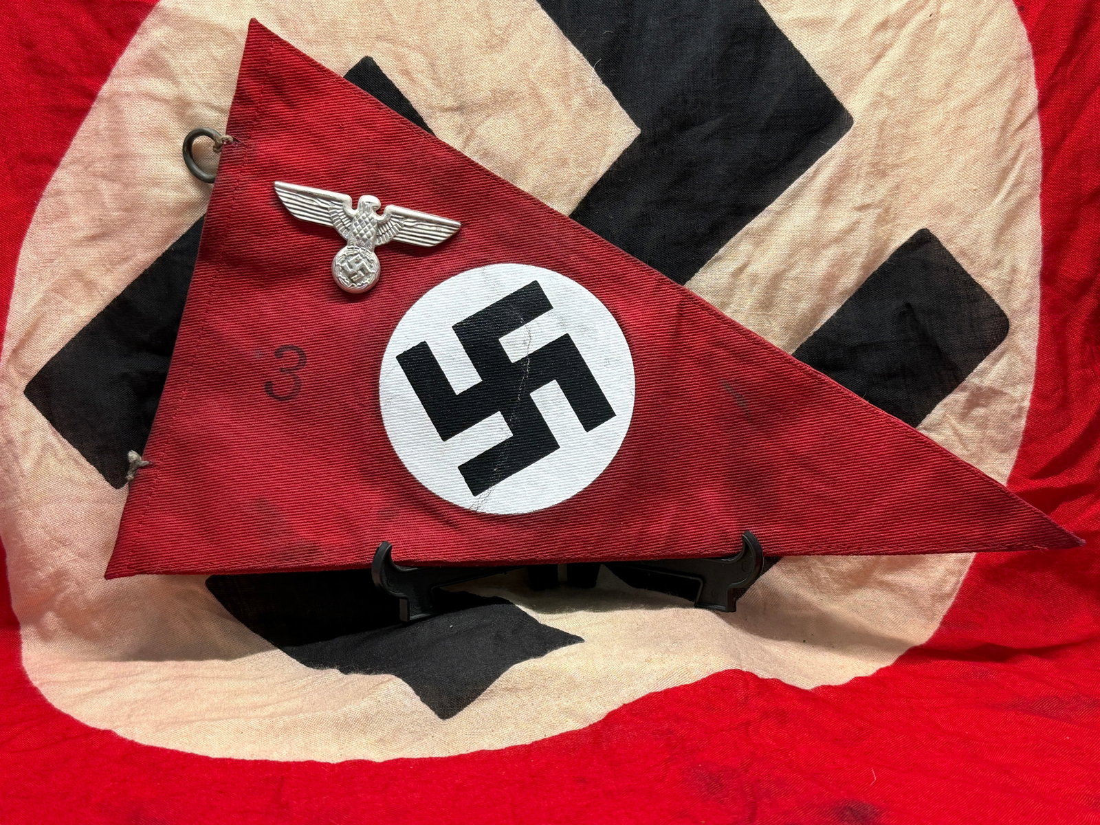 WWII German NSDAP Double-Sided Pennant: This WWII German National Socialist triangular pennant is constructed of red cloth and displays a white roundel with a black swastika on both sides. The hoist edge retains metal suspension rings for m