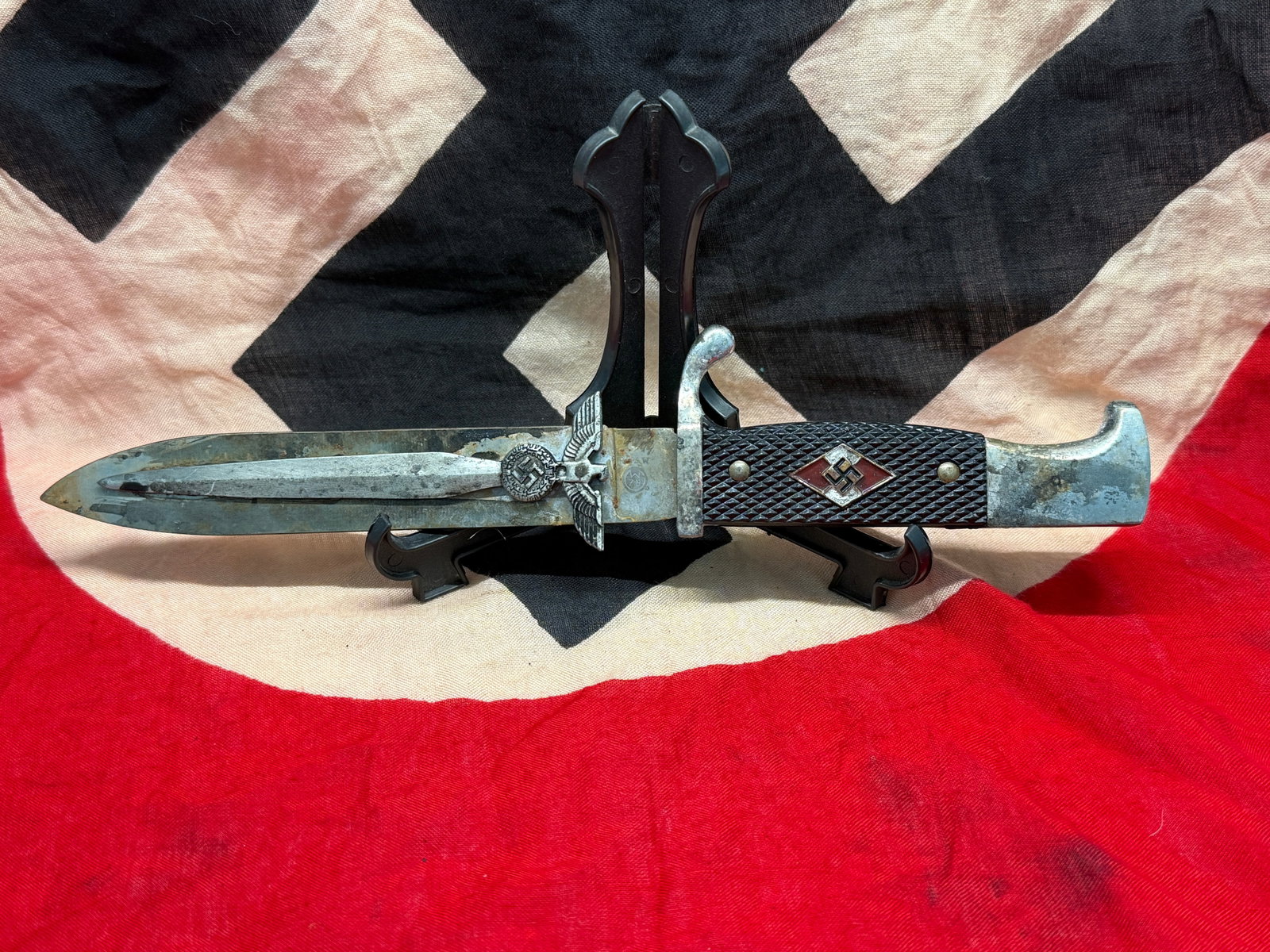 WWII German Hitler Youth Field Made Trench Knife: This knife is patterned after the standard issue edged weapon carried by members of the Hitler Youth during the Second World War. It features black checkered grip plates with the distinctive red-and-w