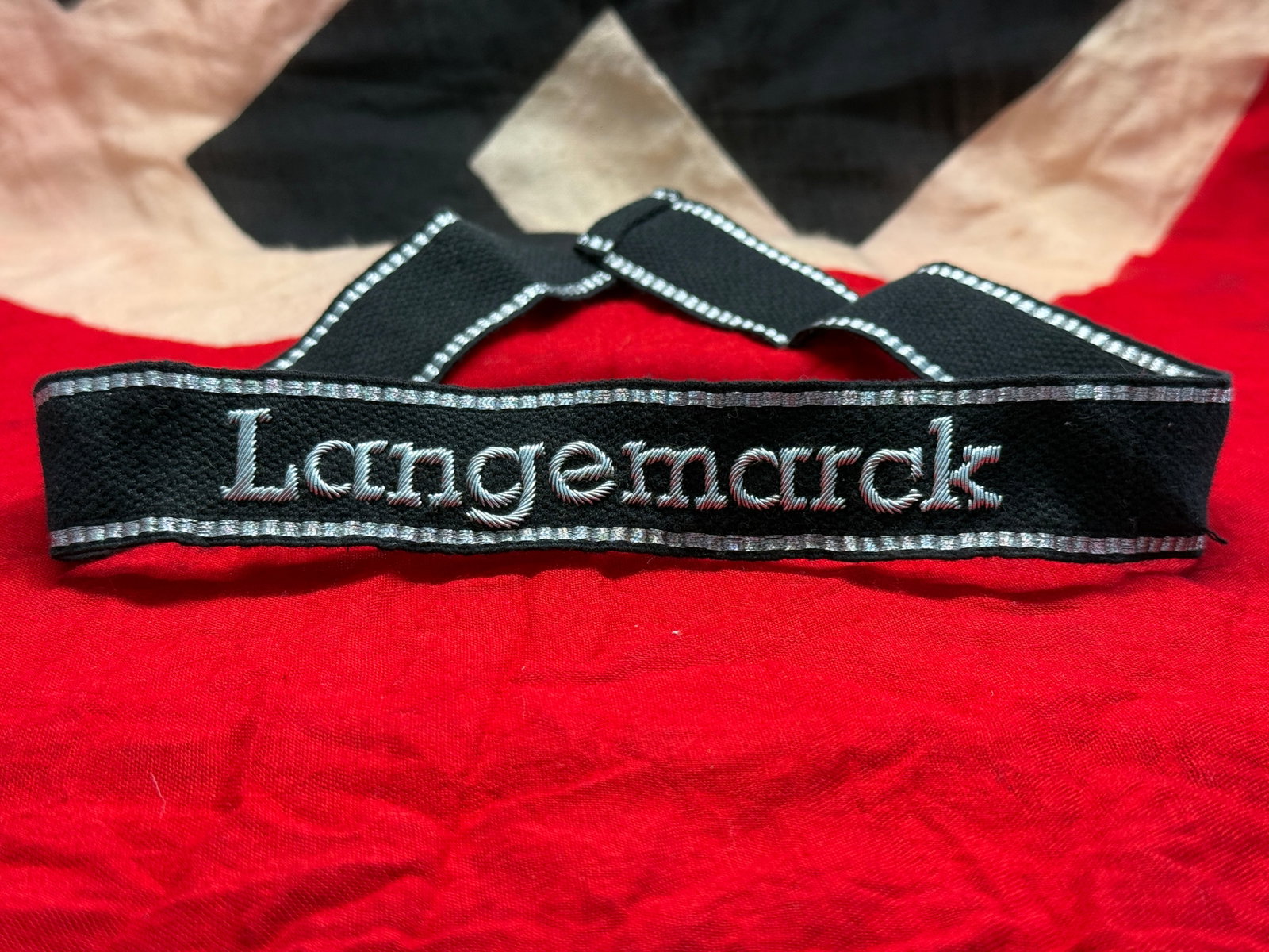 WWII German Waffen-SS "Langemarck" Cuff Title: This black woven cuff title bears the embroidered inscription "Langemarck" in silver-gray thread with matching woven borders. The title is associated with the 27th SS Volunteer Grenadier Division "Lan