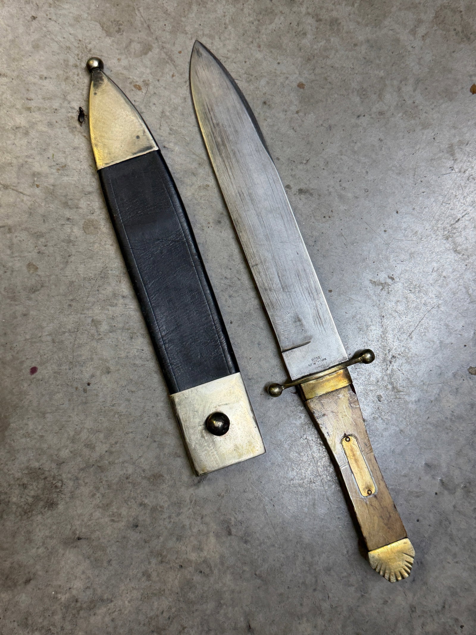1800's Rose New York Hunting Dagger with Leather Scabbard: This 1800's Hunting Dagger features a broad single-edged spear-point blade marked ROSE NEW YORK, mounted with a simple brass crossguard having rounded finials and a brass ferrule. The grip is construc