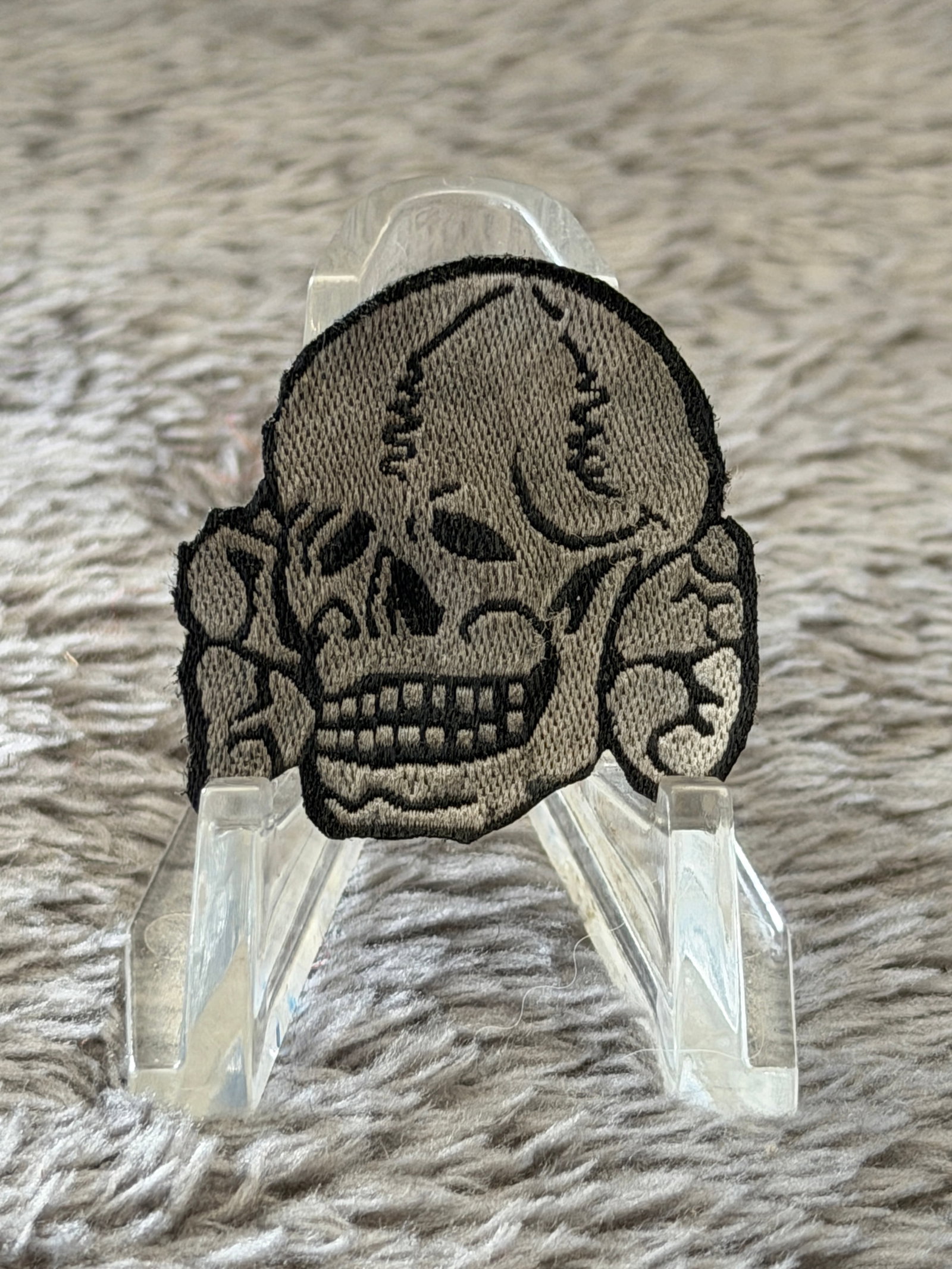 WWII German Waffen-SS Totenkopf Sleeve Insignia Patch: This WWII German Waffen-SS Totenkopf sleeve insignia patch features the iconic skull and crossed bones motif embroidered in gray and black thread on a cloth backing. The Totenkopf, or "Death's Head," 