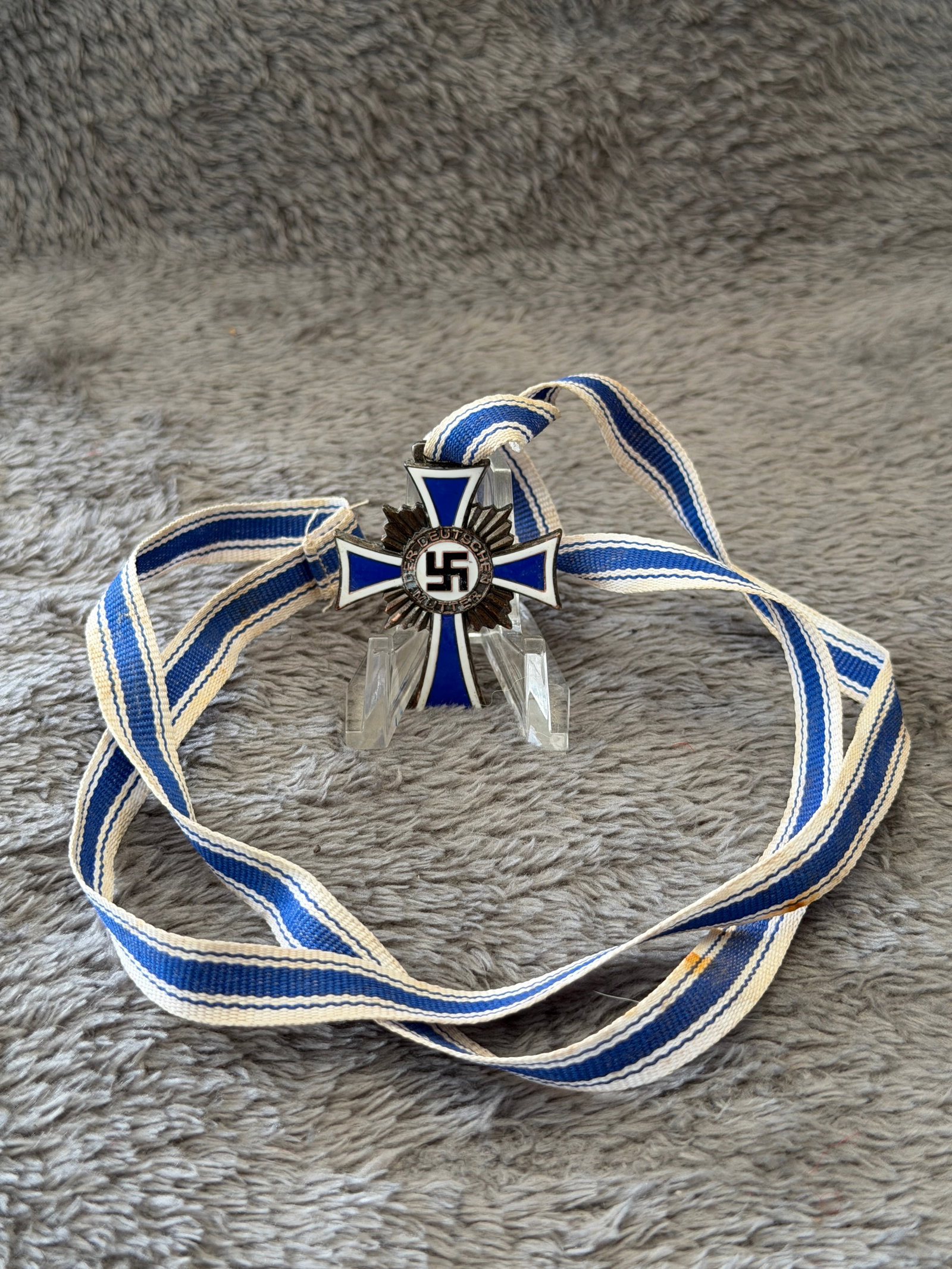 WWII German Mother's Cross (Ehrenkreuz der Deutschen Mutter) Miniature Medal with Ribbon: This WWII German Mother's Cross (Ehrenkreuz der Deutschen Mutter) miniature medal features blue and white enameled cross arms with a central black swastika encircled by the inscription "Der Deutschen 