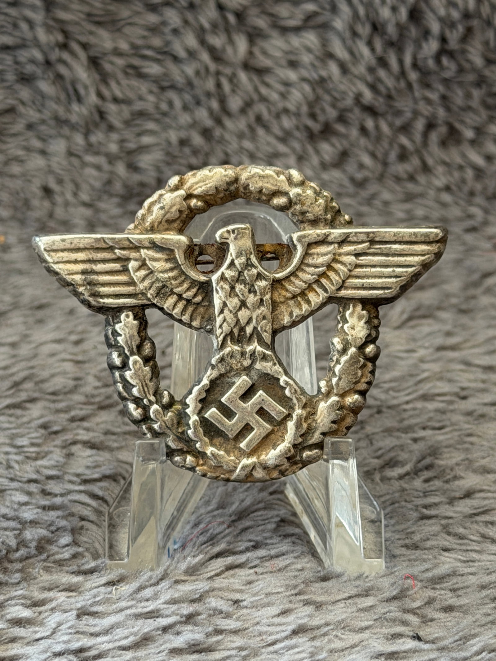 WWII German Police Eagle Wreath Cap Badge: This WWII German Police Eagle Wreath Cap Badge features the national eagle with outstretched wings above an oak leaf wreath enclosing a swastika, a design worn by members of the German Ordnungspolizei