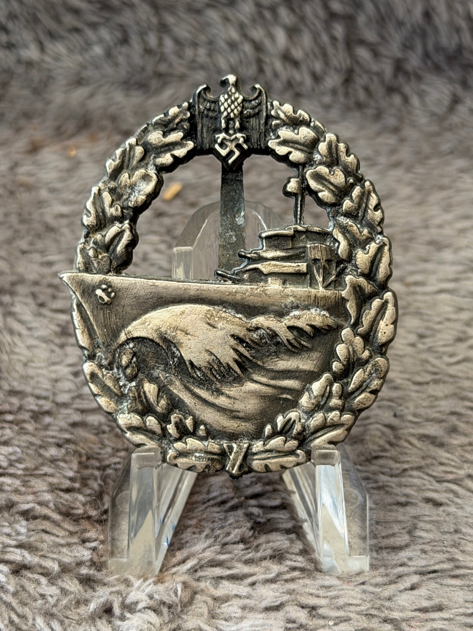 WWII German Kriegsmarine High Seas Fleet Badge: This WWII German Kriegsmarine High Seas Fleet Badge features a detailed battleship cutting through heavy seas, surrounded by an oak leaf wreath and surmounted by the national eagle clutching a wreath 