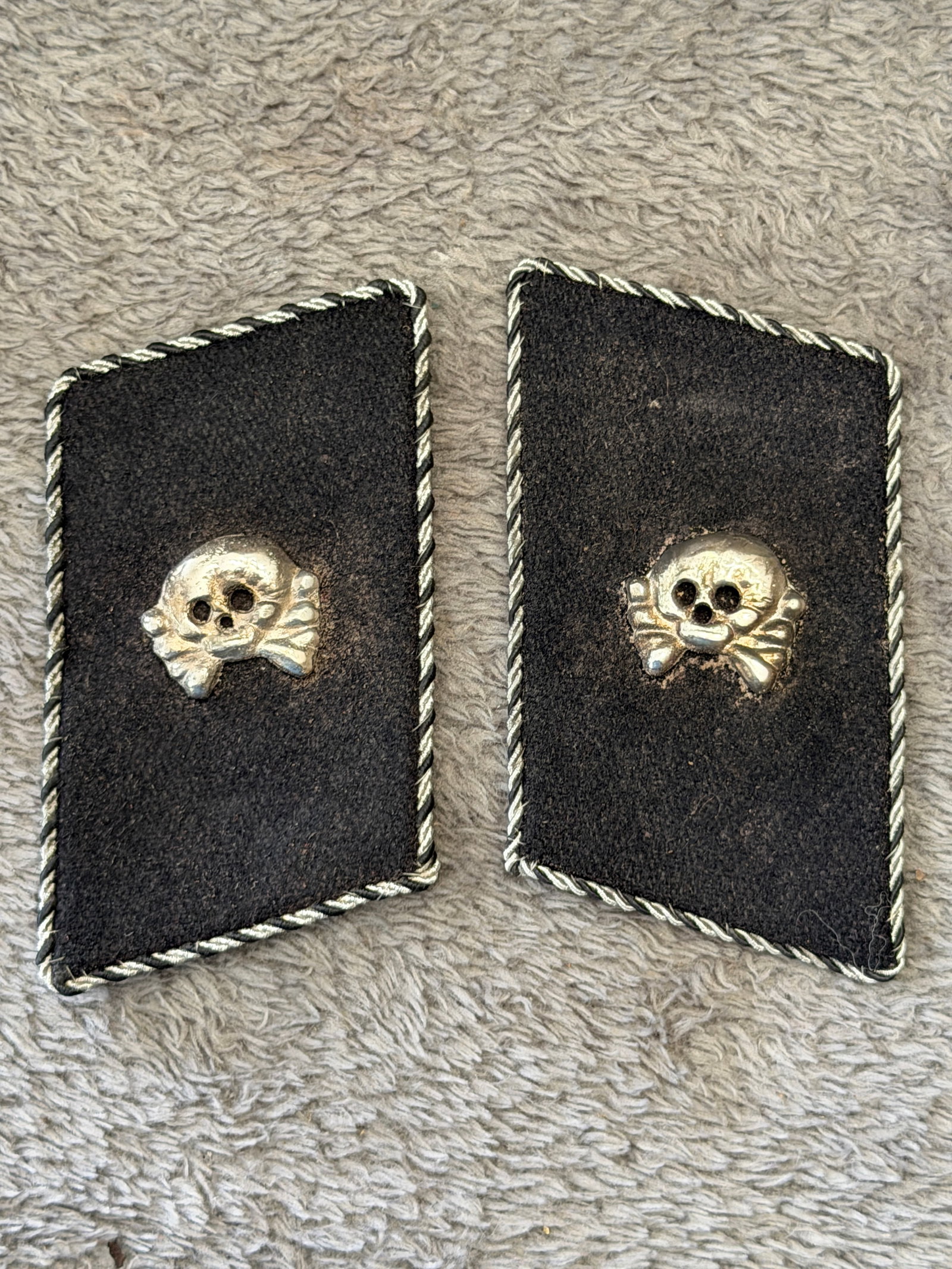 WWII German Waffen-SS Totenkopf Collar Tab Pair with RZM Tag: This WWII German Waffen-SS Totenkopf collar tab pair features the iconic silver-toned Totenkopf (Death's Head) insignia mounted on black wool tabs with twisted silver piping. One tab retains its perio
