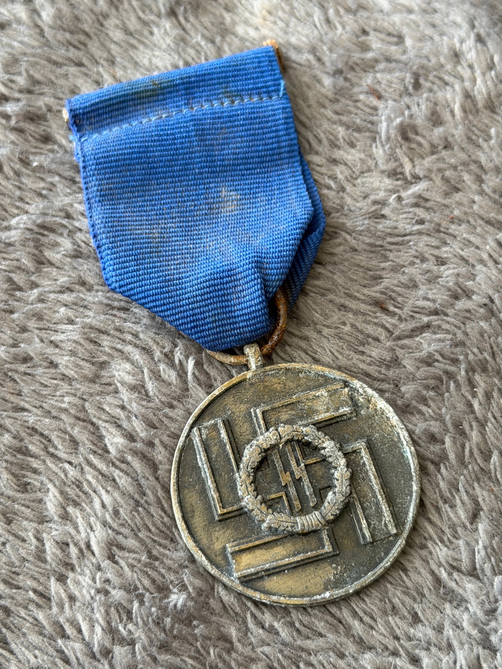 WWII German Waffen-SS Long Service Medal with Blue Ribbon: This WWII German Waffen-SS Long Service Medal features the classic blue suspension ribbon and a circular medal displaying the SS runes within an oak wreath over a large swastika on the obverse. The re