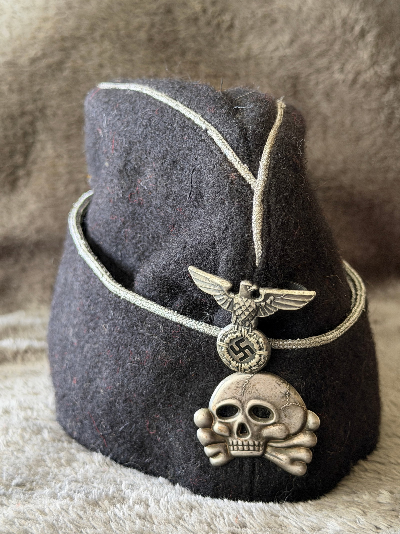 WWII German Waffen-SS EM/NCO M38 Overseas Cap with Totenkopf Insignia: This WWII German Waffen-SS M38 overseas cap (Schiffchen) is constructed of black wool with silver-white soutache piping around the crown and side fold, displaying the distinctive appearance associated