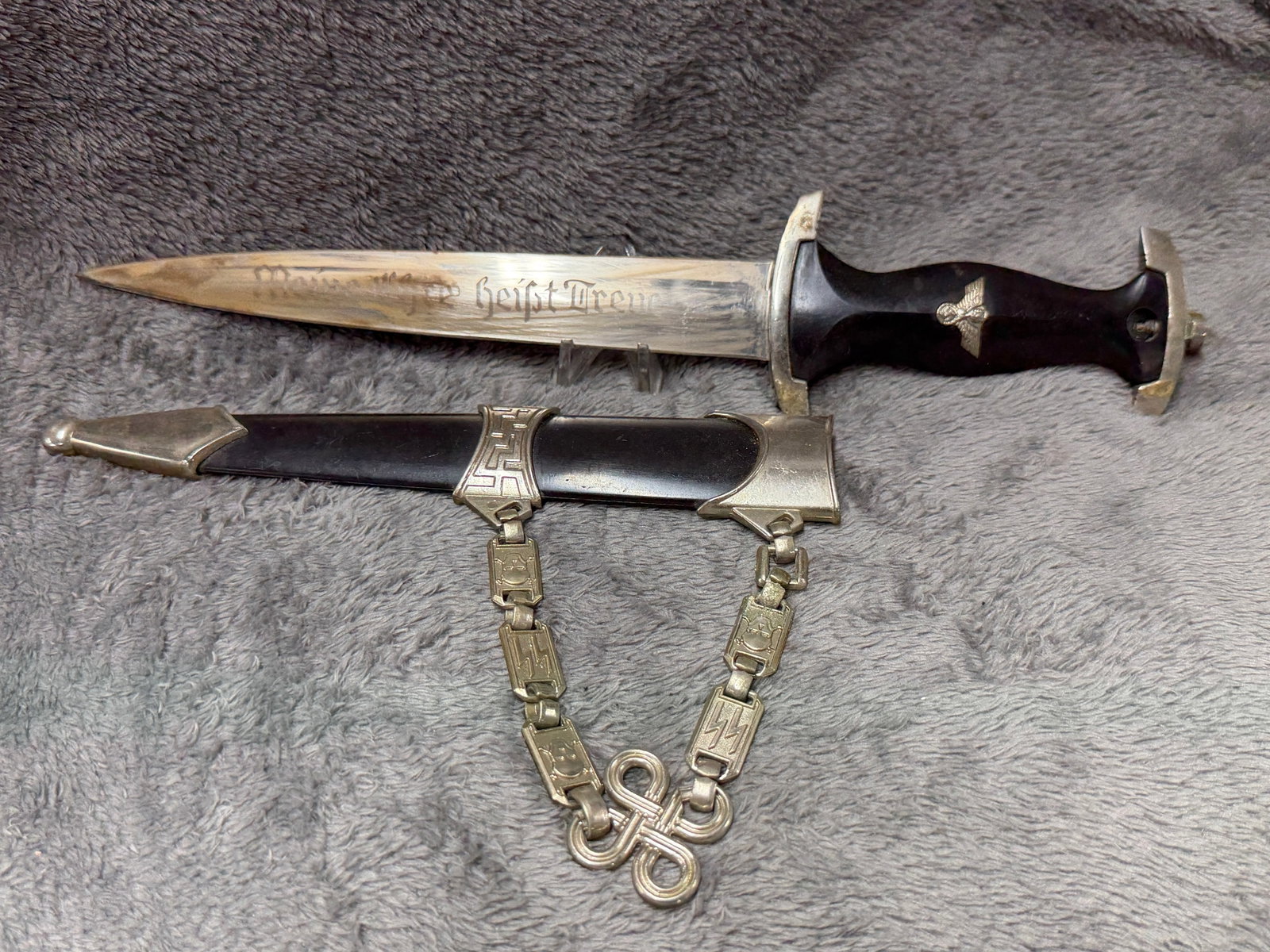 WWII German SS Motto Dagger with Scabbard & SS Hanger Chain: This WWII German SS motto dagger is accompanied by its black enameled scabbard and SS hanger chain, displaying the classic design associated with the Schutzstaffel during the Second World War. The bla