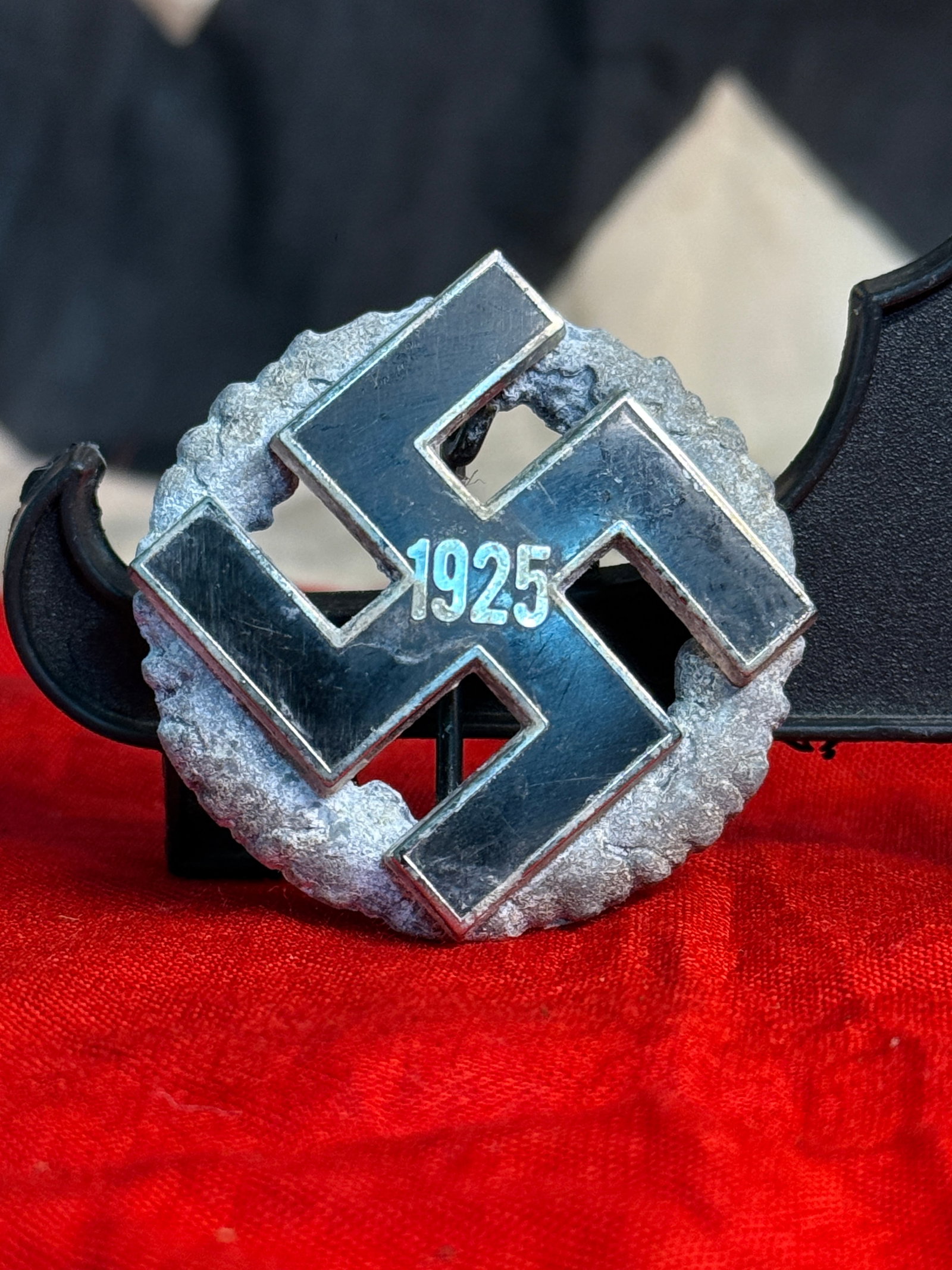 WWII German 1925 NSDAP Membership Badge: This circular enamel badge displays a black swastika with the date "1925," commemorating the re-establishment of the National Socialist German Workers' Party (NSDAP) following its reorganization. The 