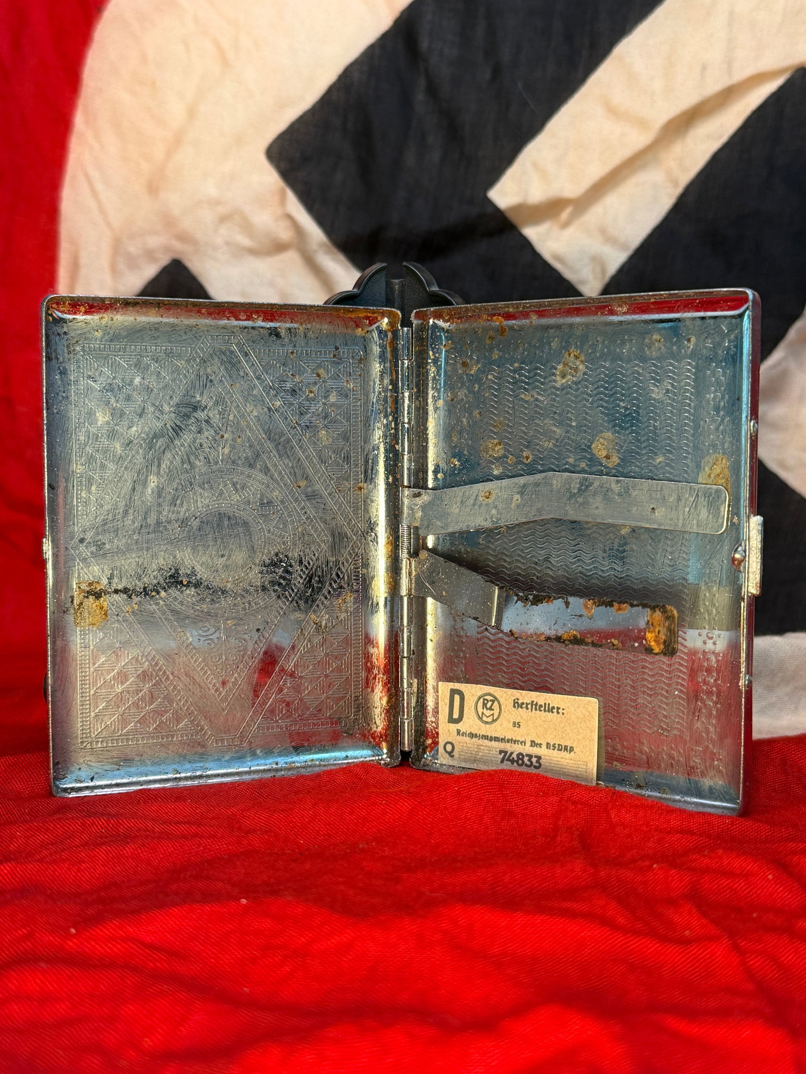 WWII German RZM-Marked NSDAP Cigarette Case: This WWII German cigarette case is constructed of plated metal with an engraved geometric interior pattern and retains its original spring-loaded cigarette retaining arms. Inside is an RZM (Reichszeug
