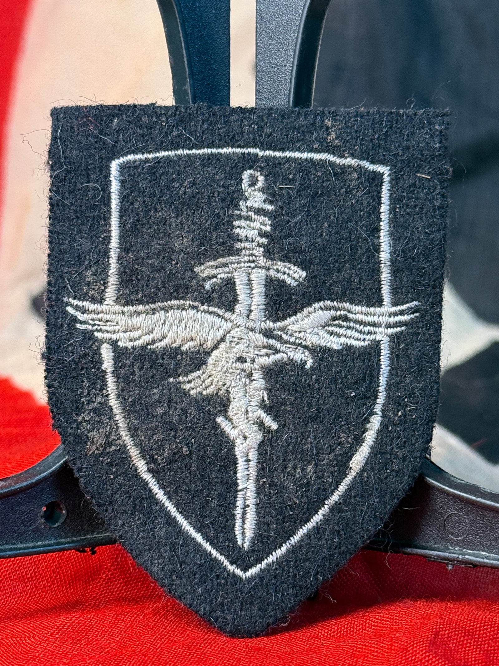 WWII German Luftwaffe Female Auxiliary (Helferin) Sleeve Patch: This WWII German Luftwaffe Female Auxiliary (Helferin) sleeve patch is embroidered in silver-gray thread on a black wool shield-shaped backing. The insignia features a vertical sword overlaid by the L