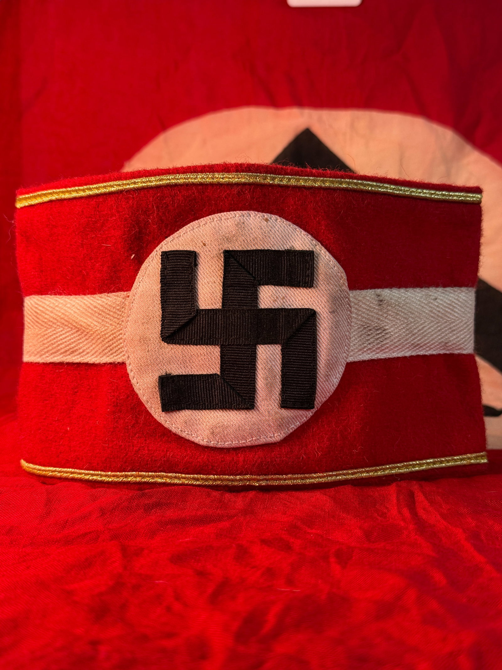 WWII German NSDAP Political Leader Armband: This WWII German NSDAP Political Leader armband is constructed of bright red wool with a white horizontal center stripe and circular white roundel bearing a black swastika, accented by gold-colored pi