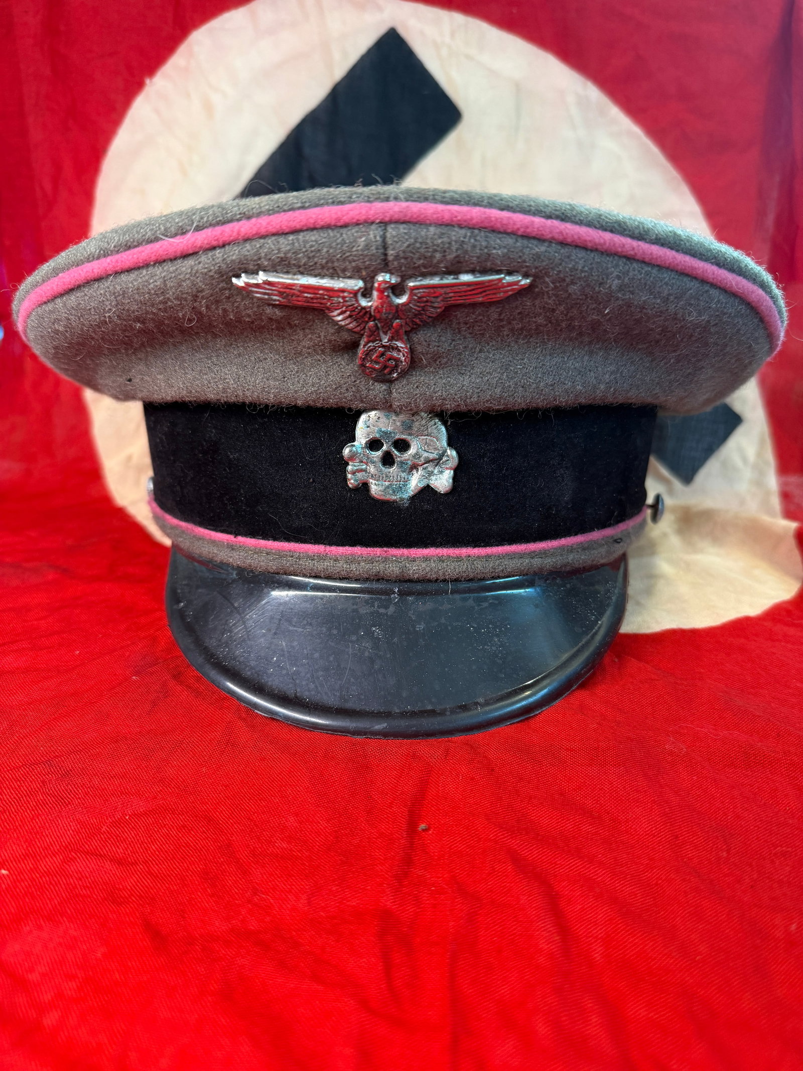 WWII German Waffen-SS Officer Visor Cap With RZM Paper Tag: This WWII German Waffen-SS officer visor cap features a field-gray wool body with pink Waffenfarbe piping, a black velvet center band, silver-colored SS Totenkopf skull, and the national eagle insigni