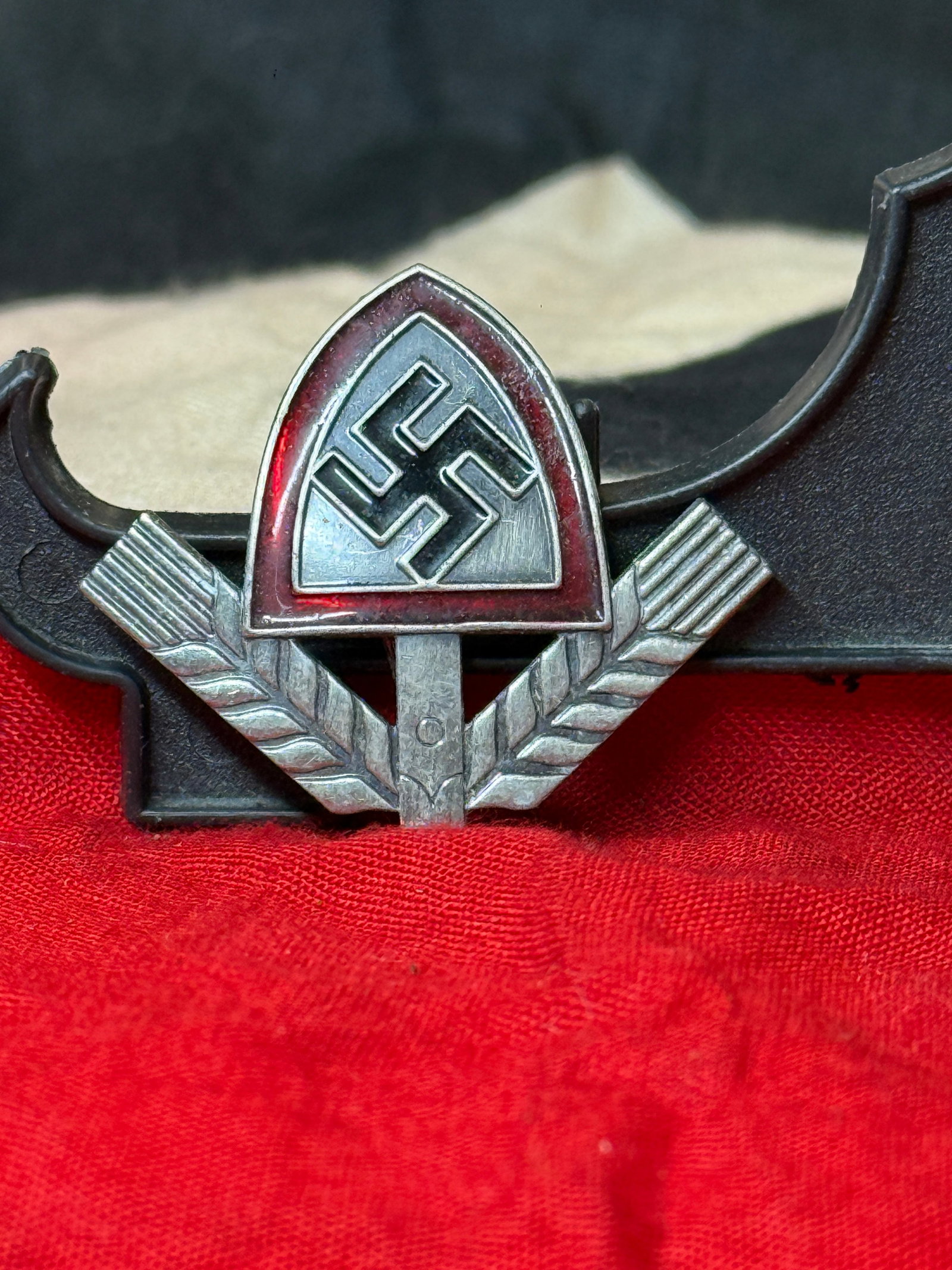 WWII German RAD Reich Labor Service Sports Badge: This WWII German Reich Labor Service (Reichsarbeitsdienst – RAD) sports badge features a red enamel triangular shield displaying a black swastika above a pair of stylized wheat sheaves. The reverse 
