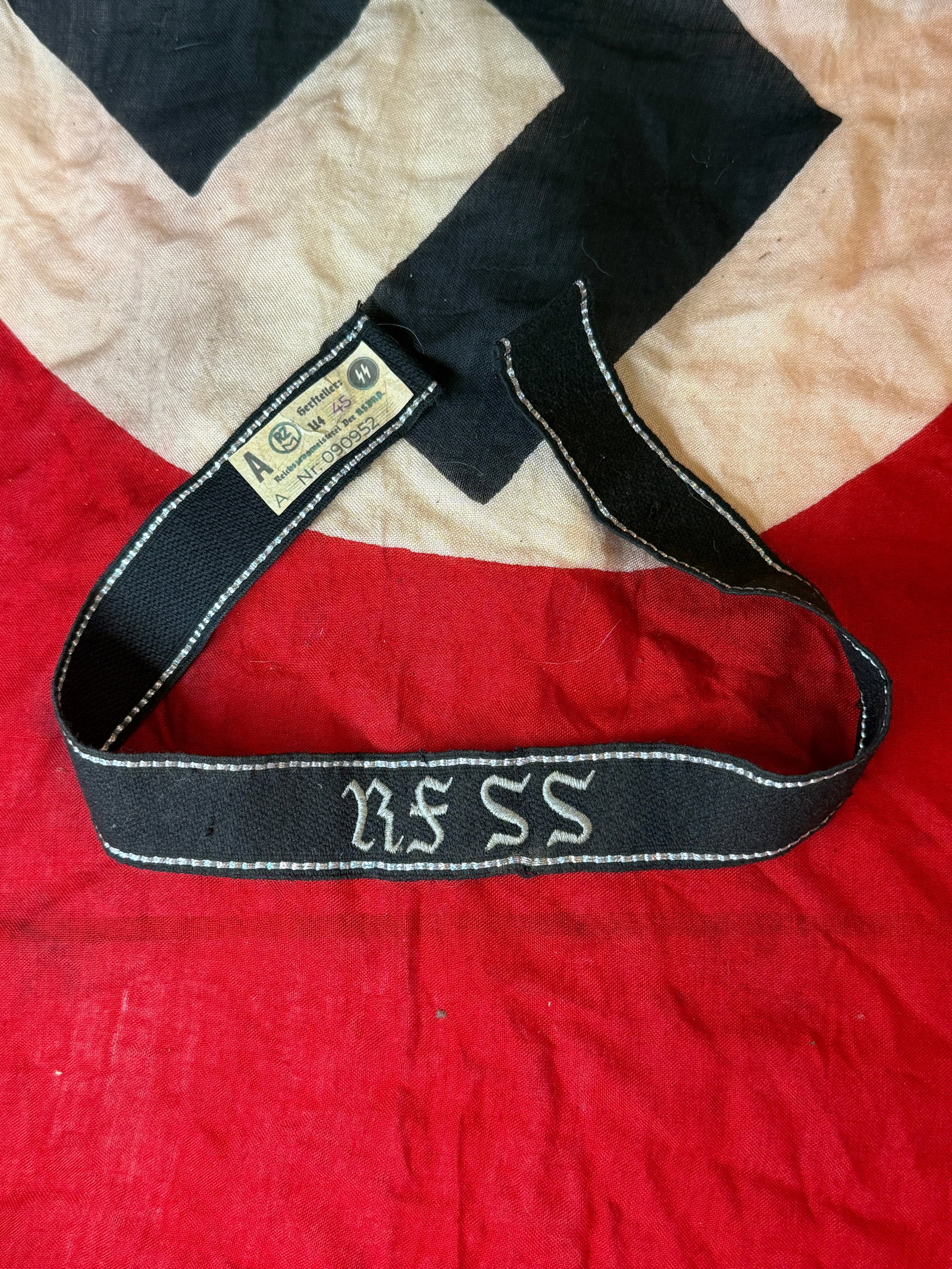 WWII German Waffen-SS Cuff Title With RZM Paper Tag: This WWII German Waffen-SS cuff title is constructed of black woven fabric with silver borders and embroidered "SS" runes. The interior retains its original RZM paper control label, marked with approv