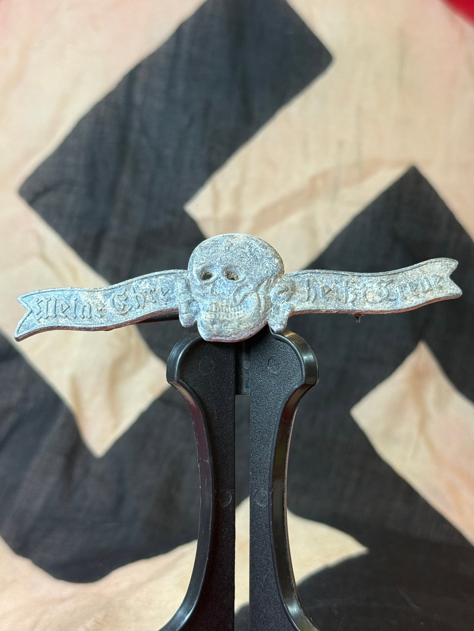 WWII German Waffen-SS Totenkopf Motto Badge By RZM M1/34: This WWII German Waffen-SS Totenkopf motto badge is cast in silver-colored metal and depicts the iconic skull and crossbones with flowing banners bearing the inscription "Meine Ehre heißt Treue" ("My