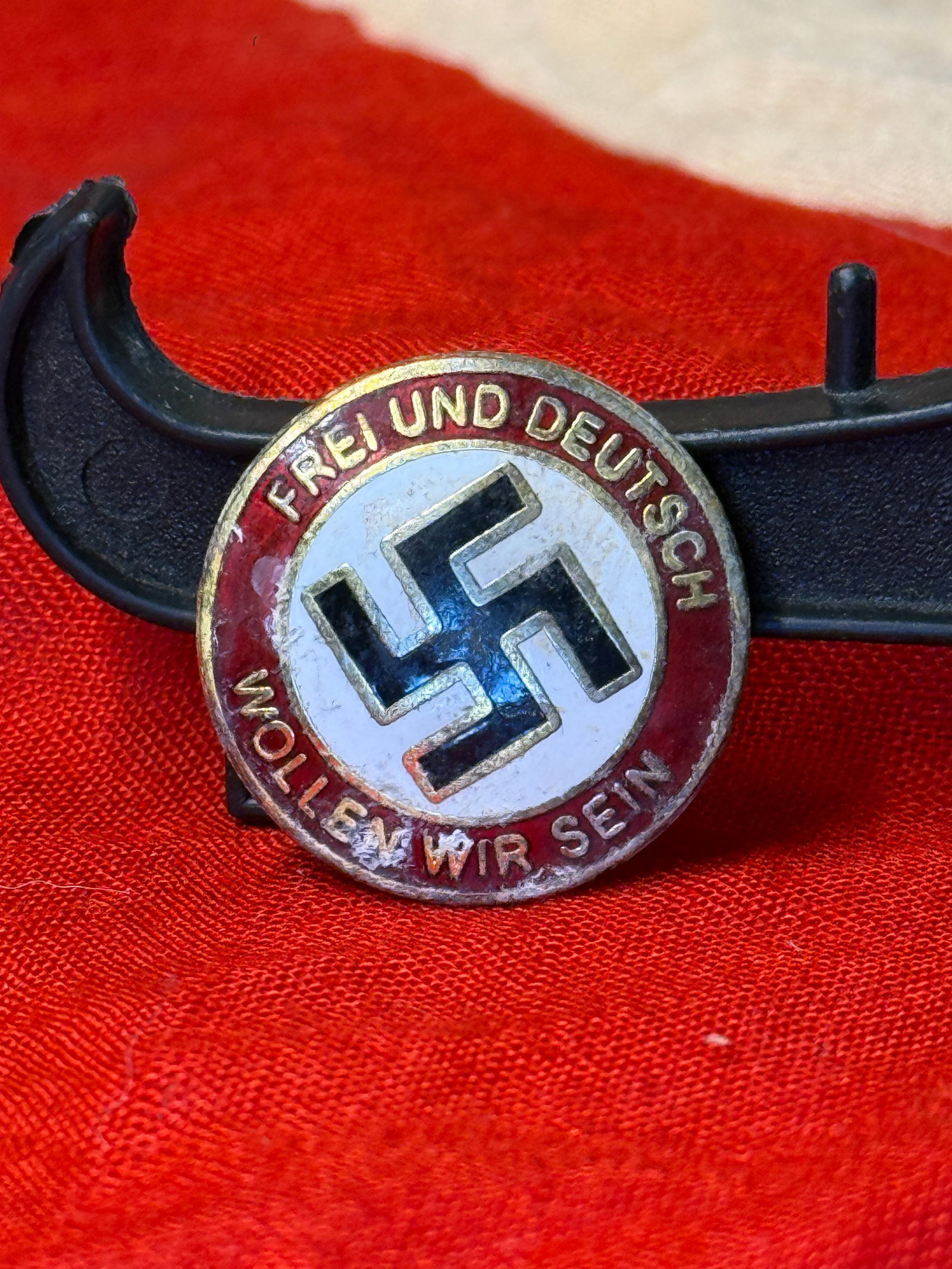 WWII German NSDAP "Frei und Deutsch – Wollt Ihr Sein" Membership Badge: This circular WWII German National Socialist German Workers' Party (NSDAP) badge features a black swastika on a white enamel field surrounded by a red enamel border bearing the slogan "FREI UND DEUTSC