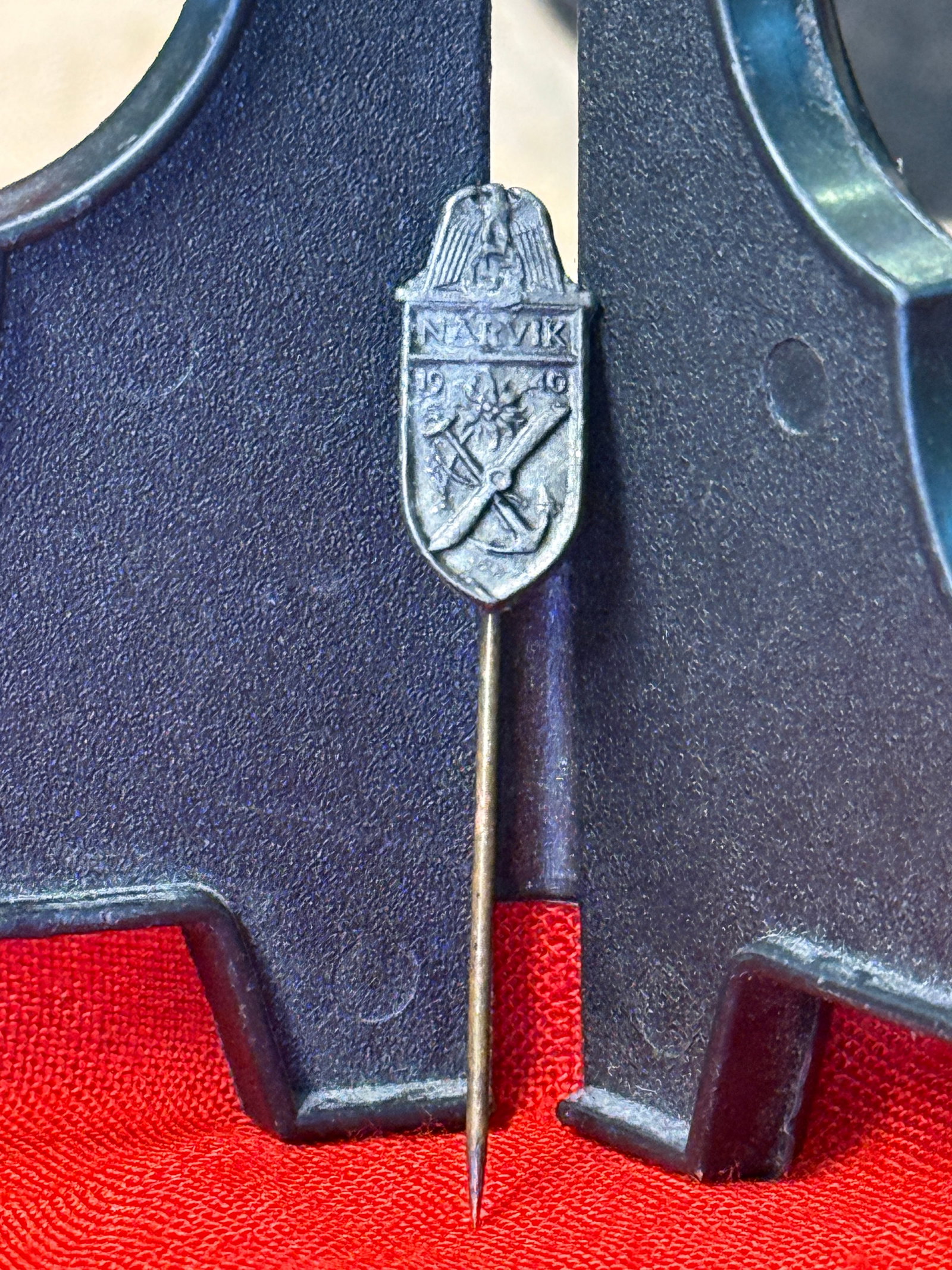 WWII German Narvik Campaign Commemorative Stickpin: This miniature WWII German stickpin commemorates the 1940 Narvik Campaign in Norway and features a shield bearing the inscription "NARVIK," crossed weapons, an edelweiss flower, and the date "1940" be