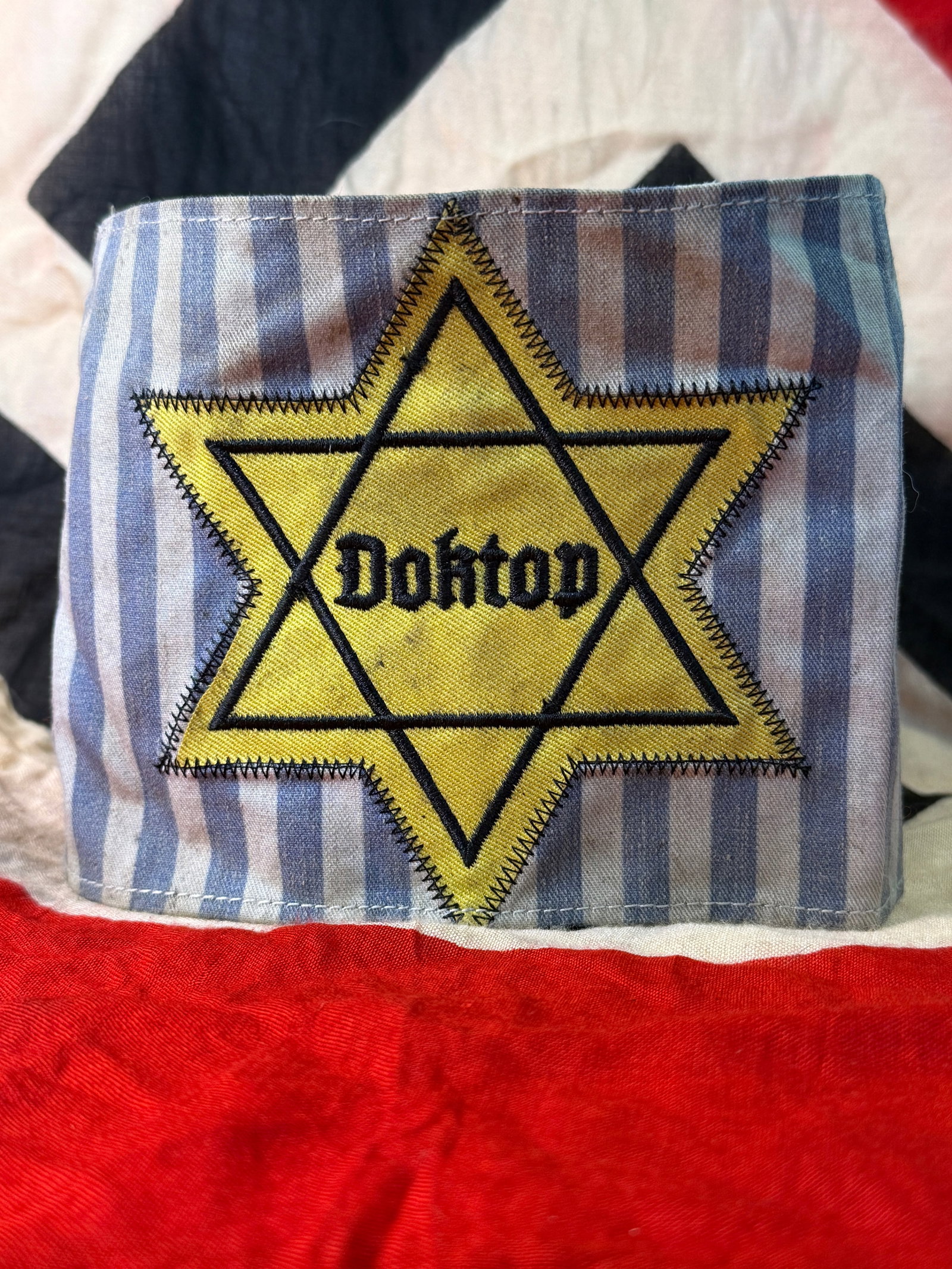 WWII Holocaust Concentration Camp Prisoner Armband – Yellow Star of David “Dohtop?? Striped: WWII/Holocaust-related striped cloth armband featuring a large yellow Star of David outlined in black and bearing the word “Dohtop” in black Gothic-style lettering across the center. The armba