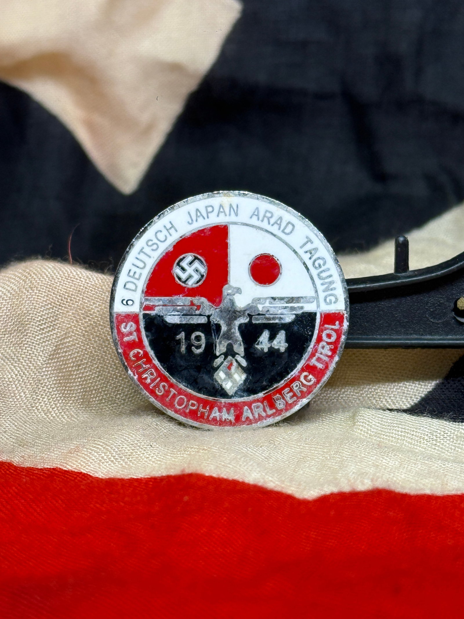 WWII German–Japanese Friendship Meeting Badge – 6th Deutsch Japan Arlberg Conference 1944 By RZM: This circular enameled commemorative badge was issued for the 6. Deutsch Japan Tagung (German-Japanese Conference) held at St. Christoph am Arlberg, Tirol in 1944. The obverse features the national em