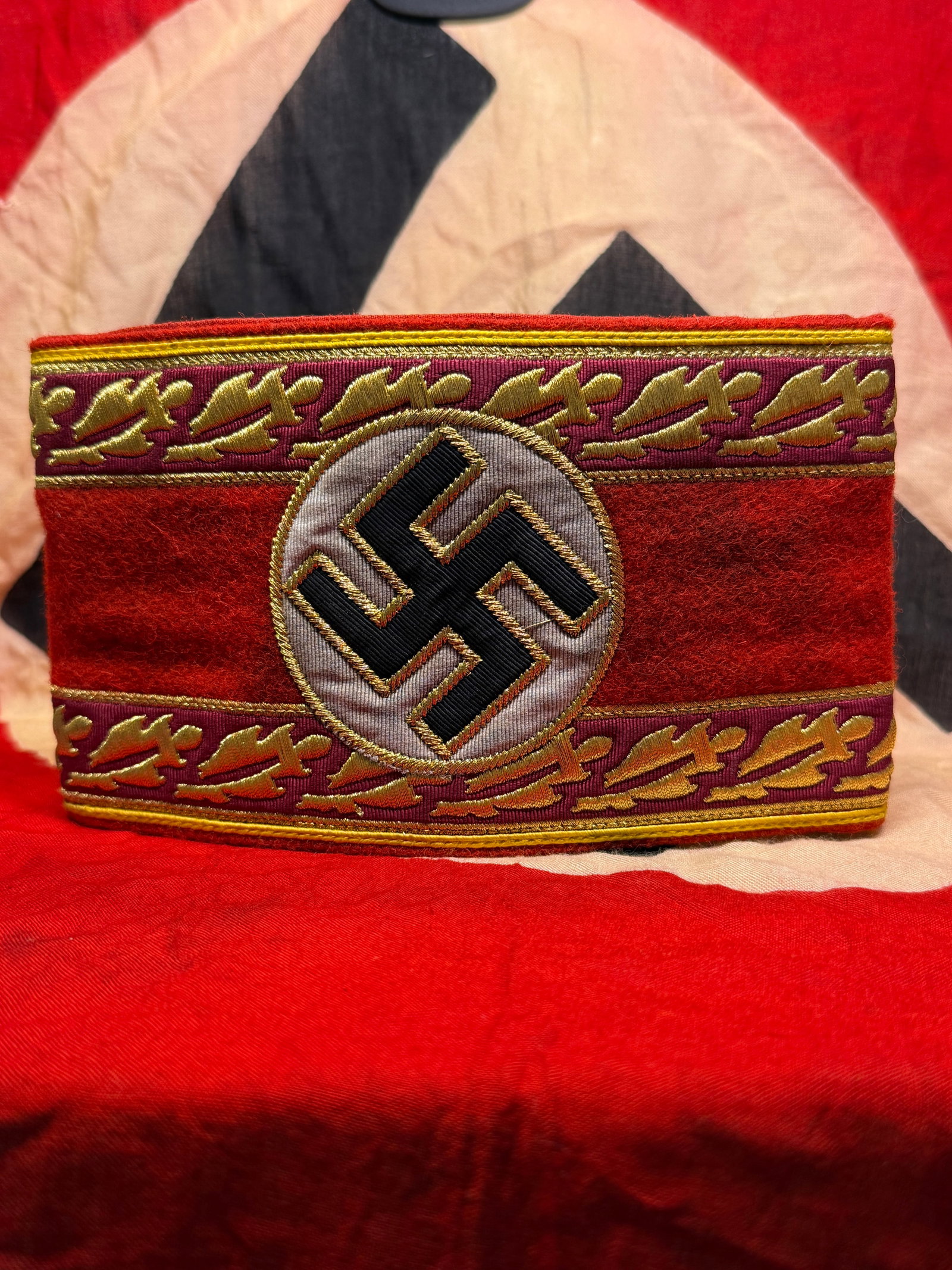 WWII German NSDAP Political Leader Armband With RZM Paper Tag: This red wool NSDAP Political Leader armband features a separately applied white roundel with black swastika and distinctive gold embroidered oak leaf borders denoting political leadership status. The